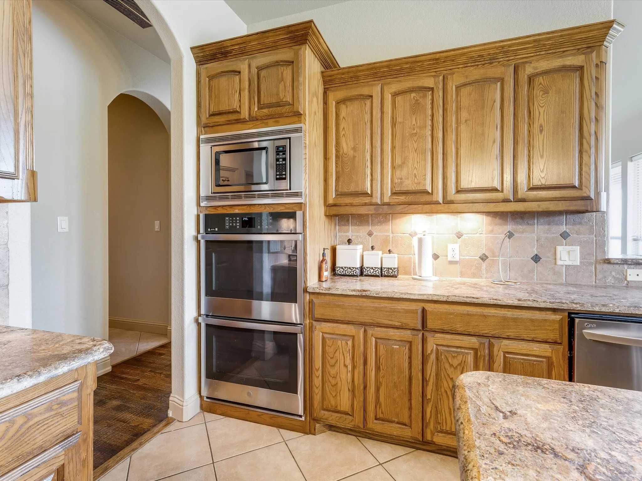 Kitchen featuring wood cabinetry, stainless steel built-in microwave and double ovens, tile backsplash, and stone-finish countertops