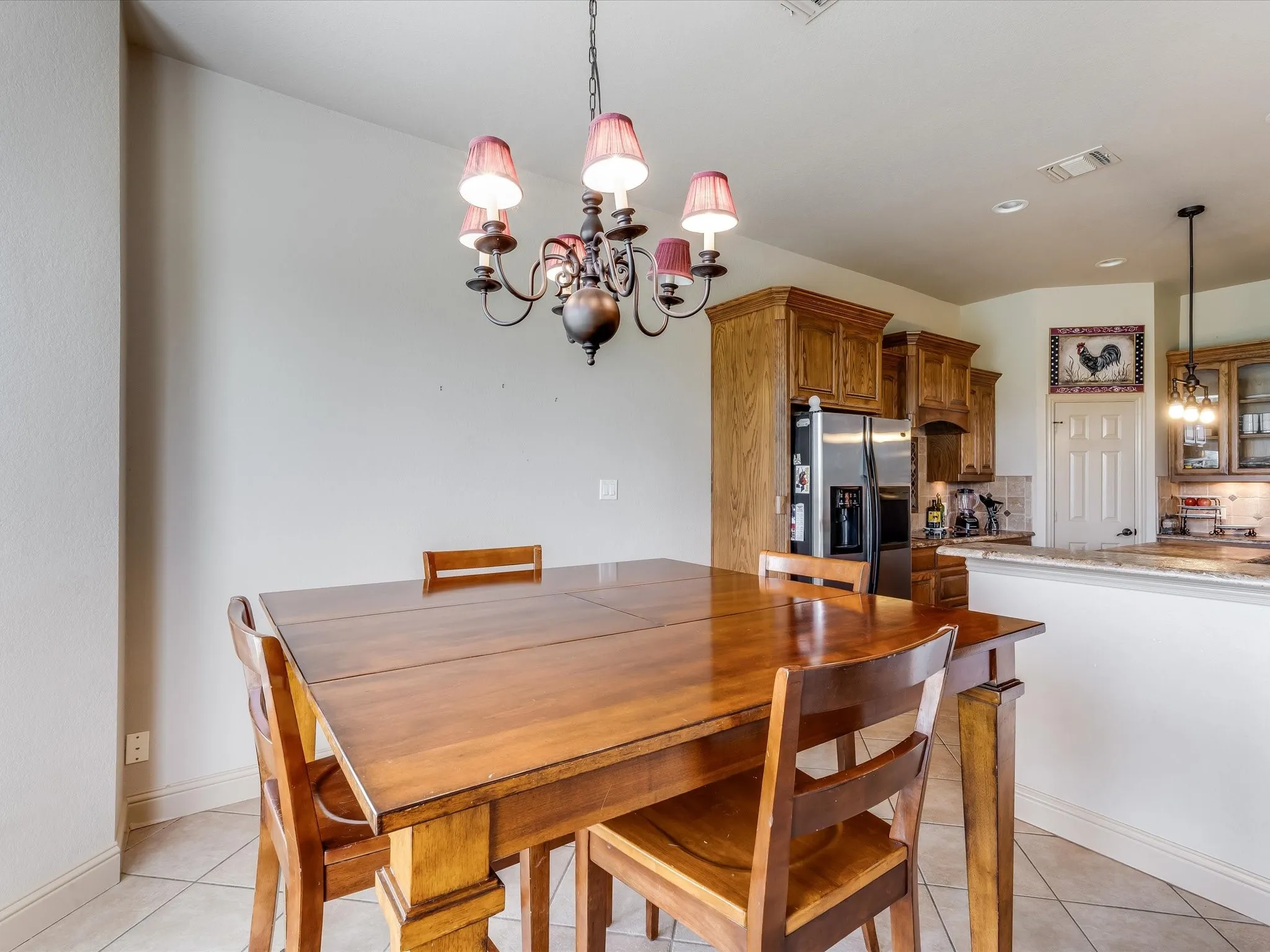 Dining area featuring a decorative chandelier with shaded lights, tiled flooring, and a kitchen pass-through with a granite-style countertop