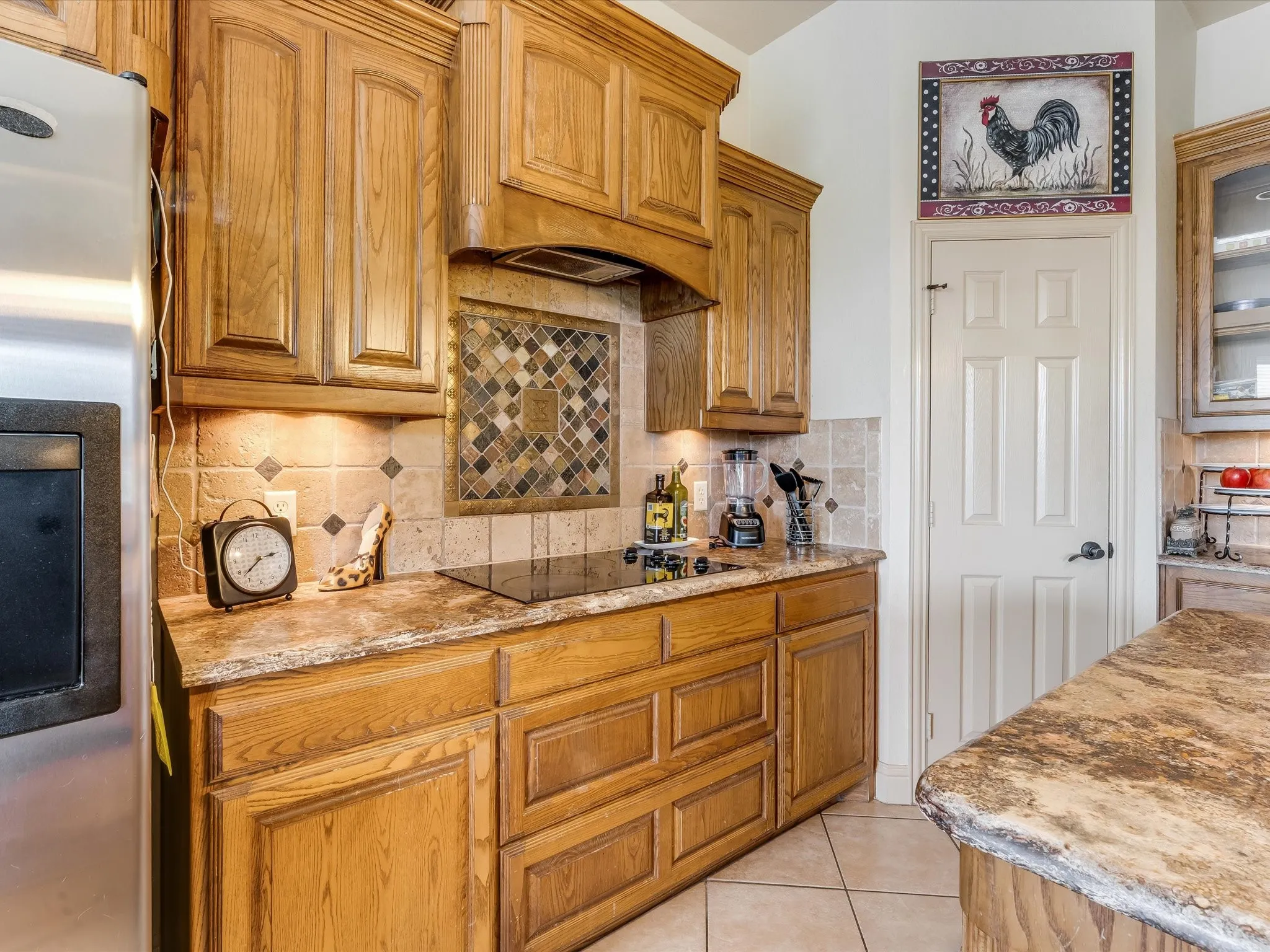 Kitchen featuring wood cabinetry, stone countertops, a tile backsplash with a decorative inset, and an integrated cooktop