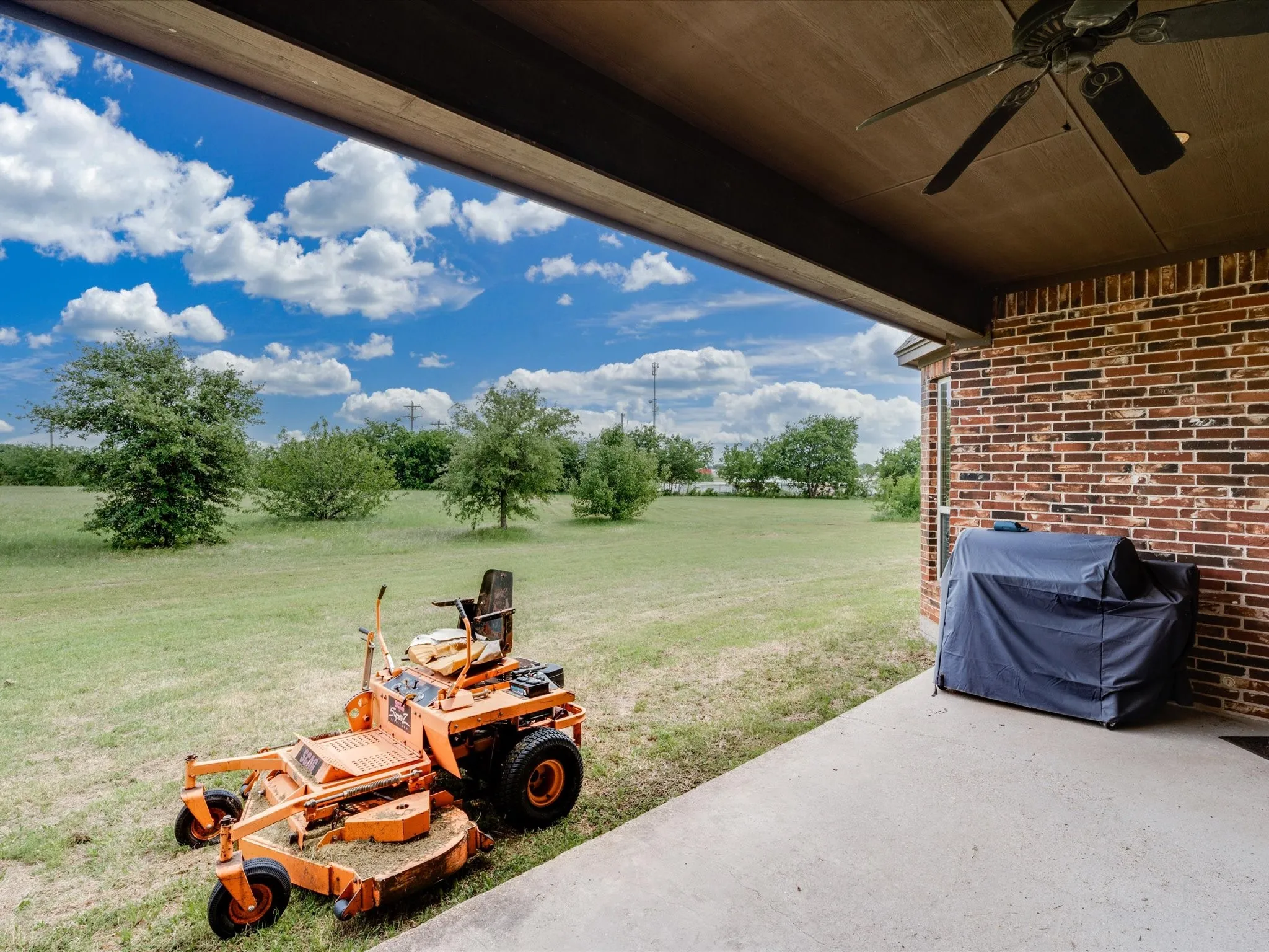 Covered patio featuring a ceiling fan, concrete flooring, and a brick exterior wall