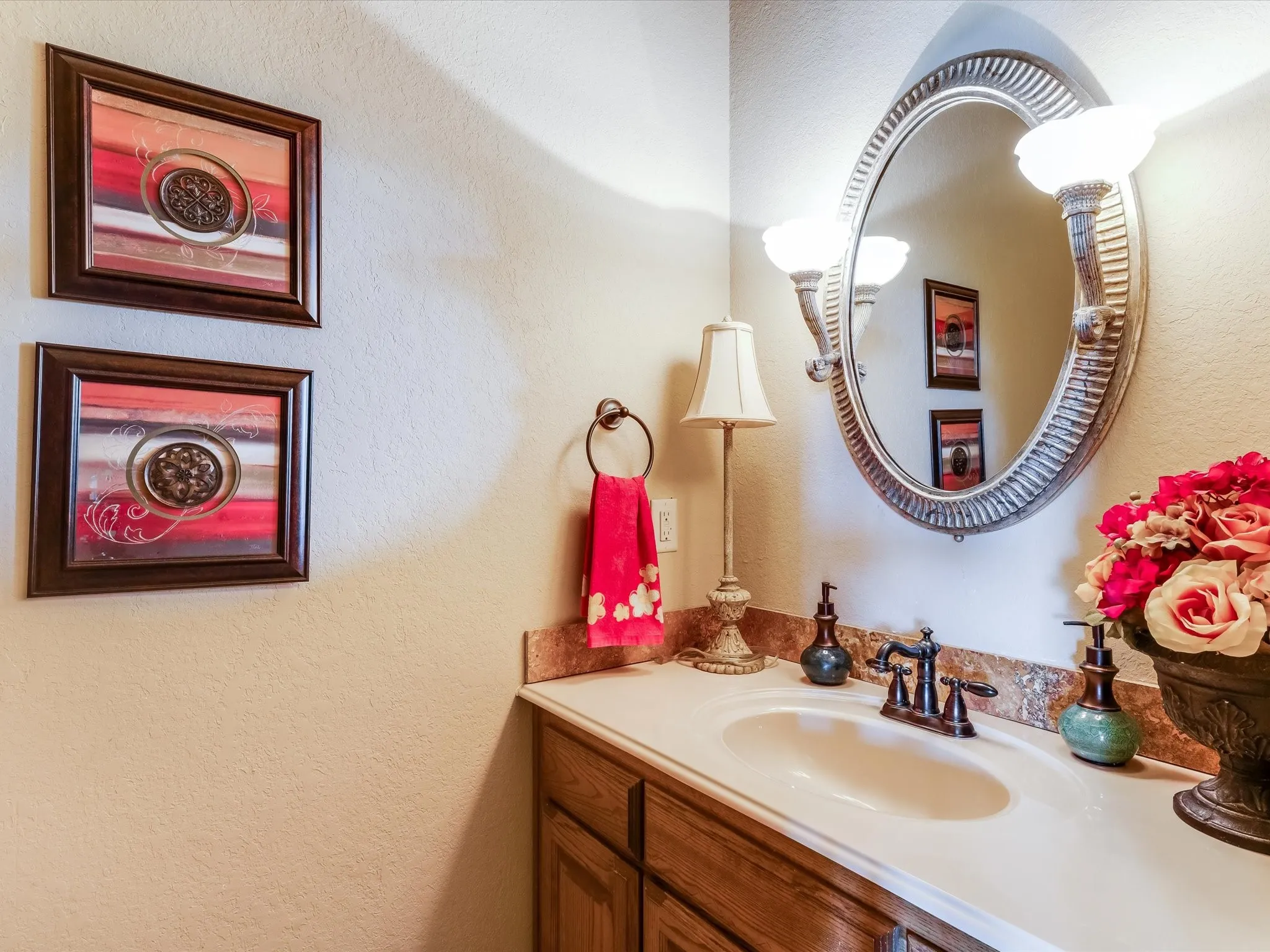 Bathroom vanity featuring a white oval sink, bronze-finish faucet, and an ornate framed mirror with sconce lighting
