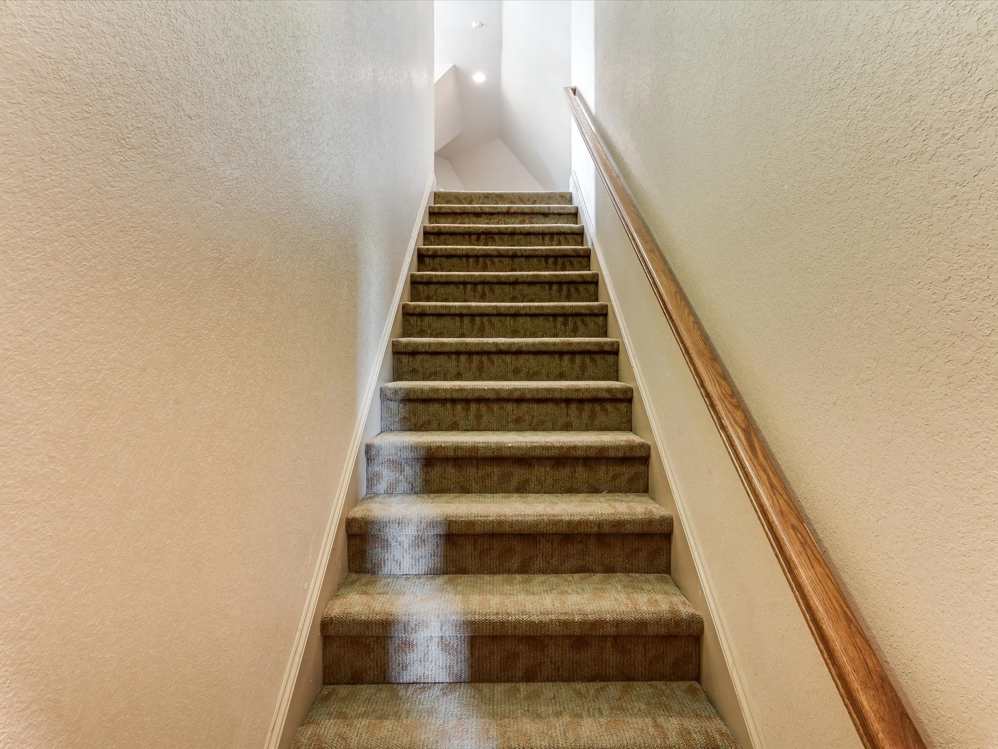 Carpeted staircase with a natural wood-finish handrail, textured walls, and recessed lighting
