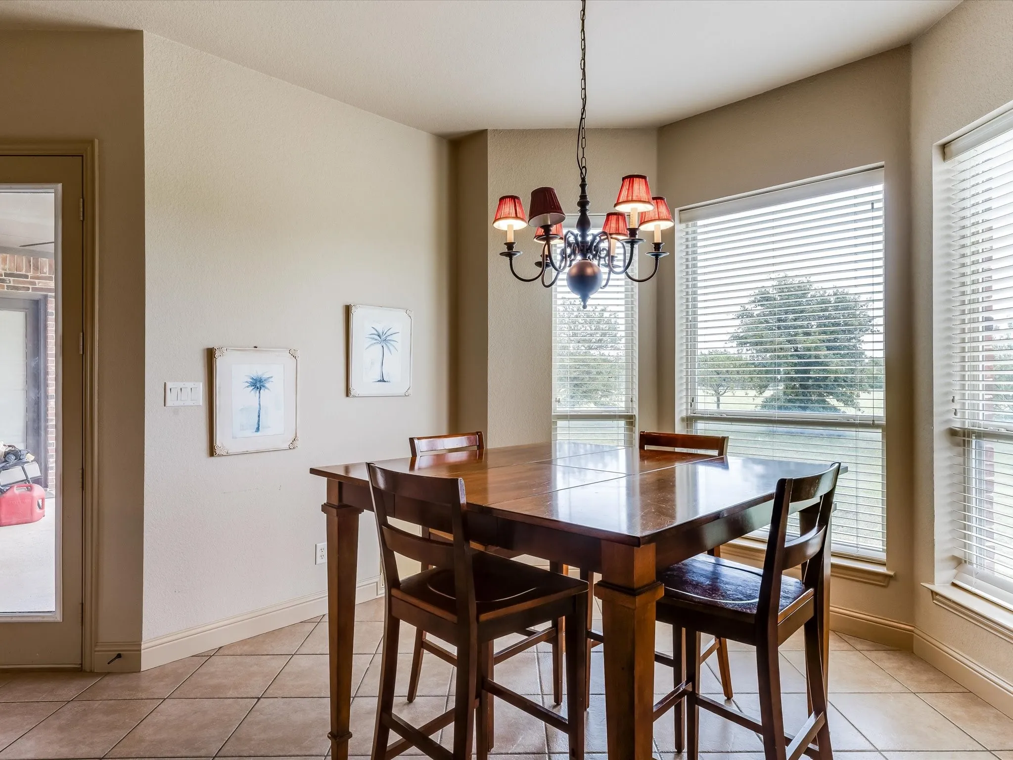 Dining area featuring a decorative chandelier with red shades, bay windows with horizontal blinds, and tile flooring with a diagonal pattern