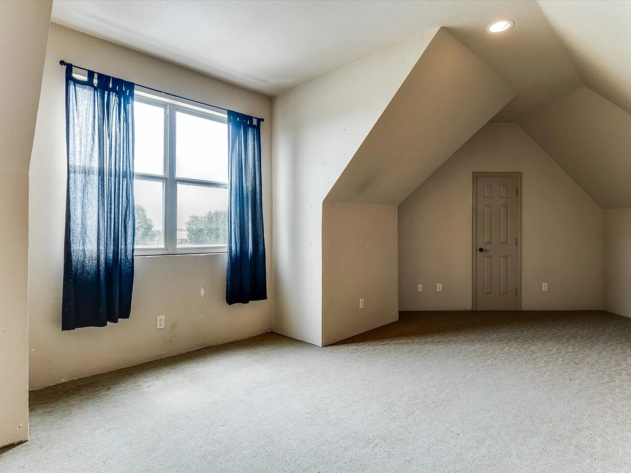 Carpeted room featuring a double-paned window, sloped ceilings, and a recessed ceiling light fixture