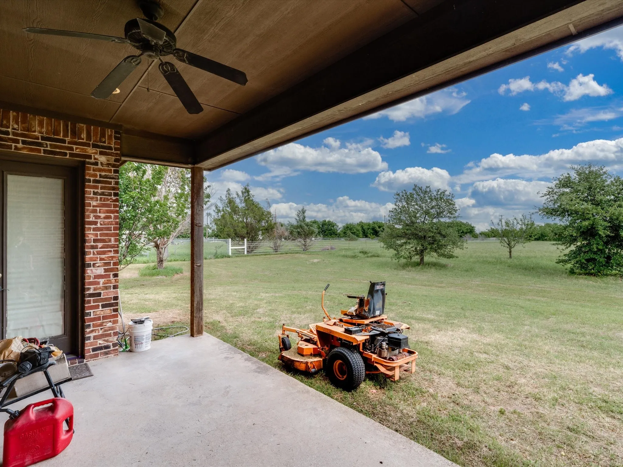 Covered back patio with a ceiling fan, concrete flooring, and brick exterior
