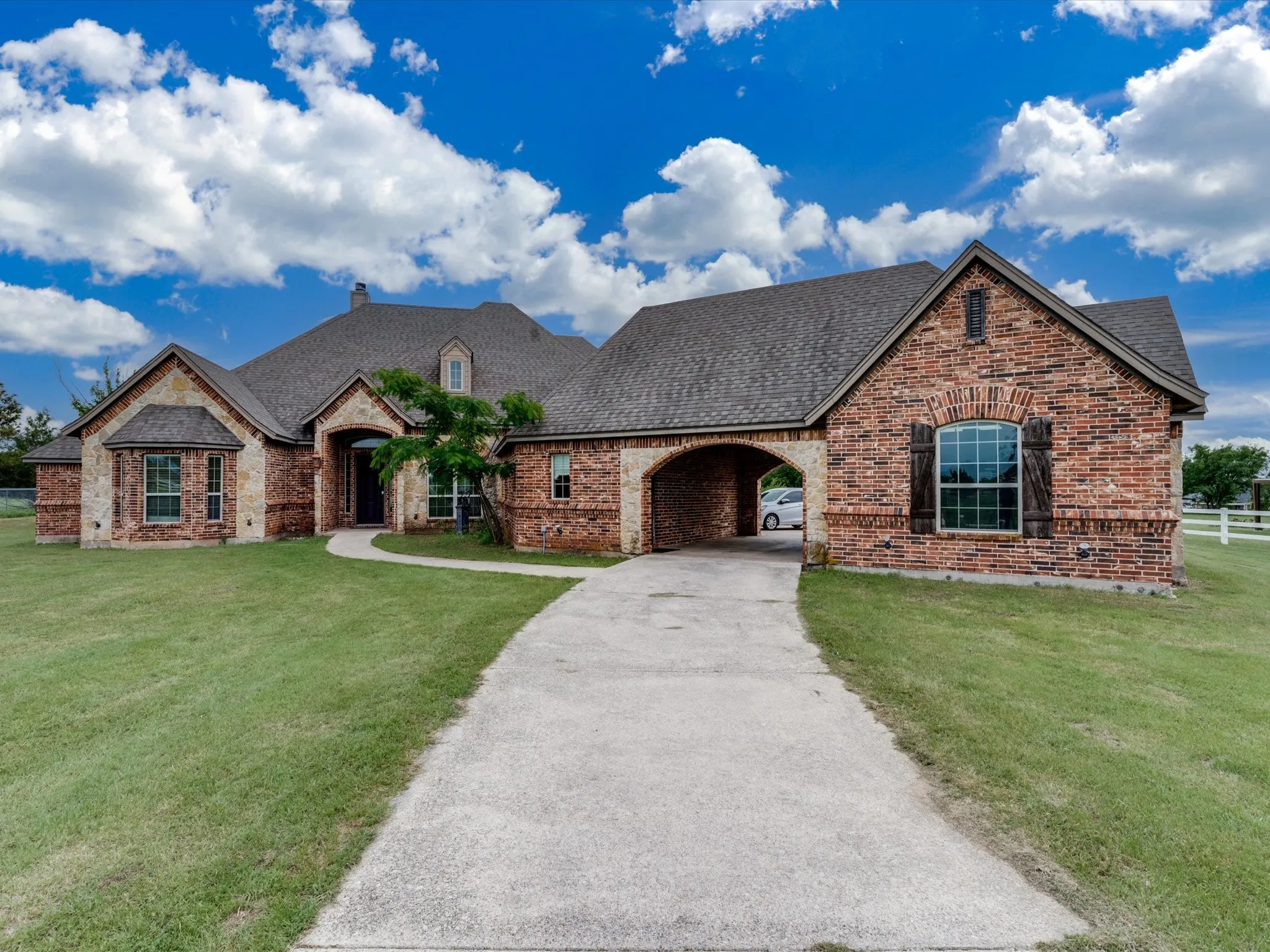 Brick and stone facade residence featuring a covered entryway, arched port-cochere, and a concrete driveway
