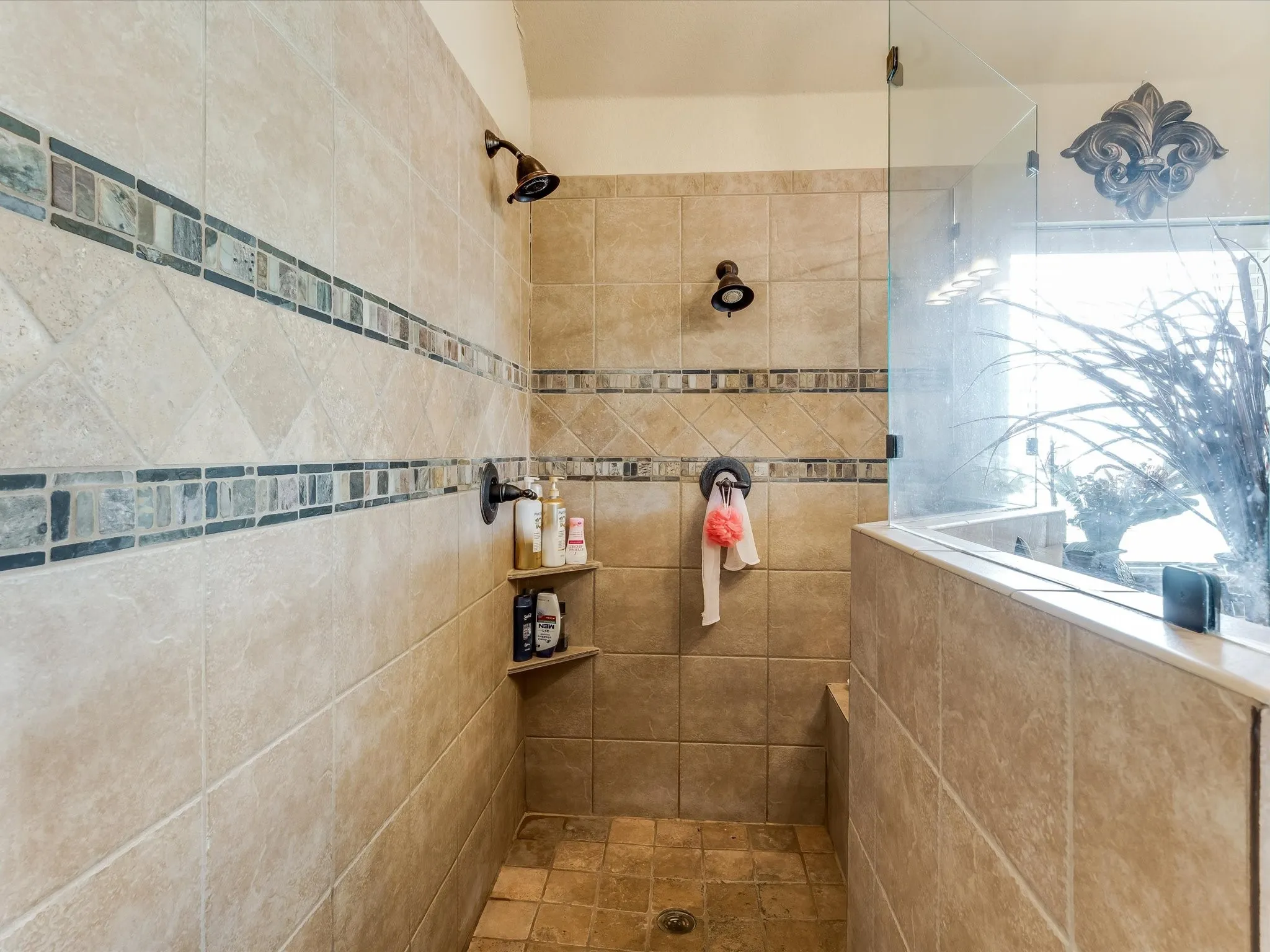 Tiled shower enclosure featuring dual showerheads, glass paneling, an integrated half-wall, and built-in corner shelving