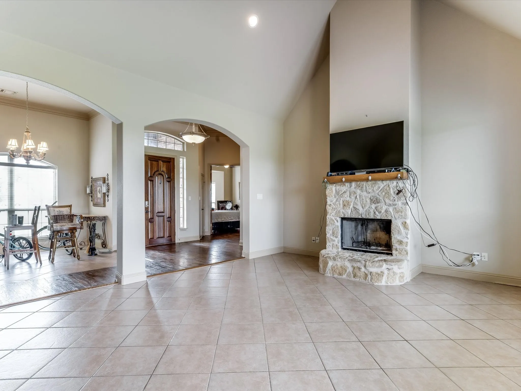 Spacious room featuring tile flooring, a prominent stone fireplace with a wood mantle, and high vaulted ceilings
