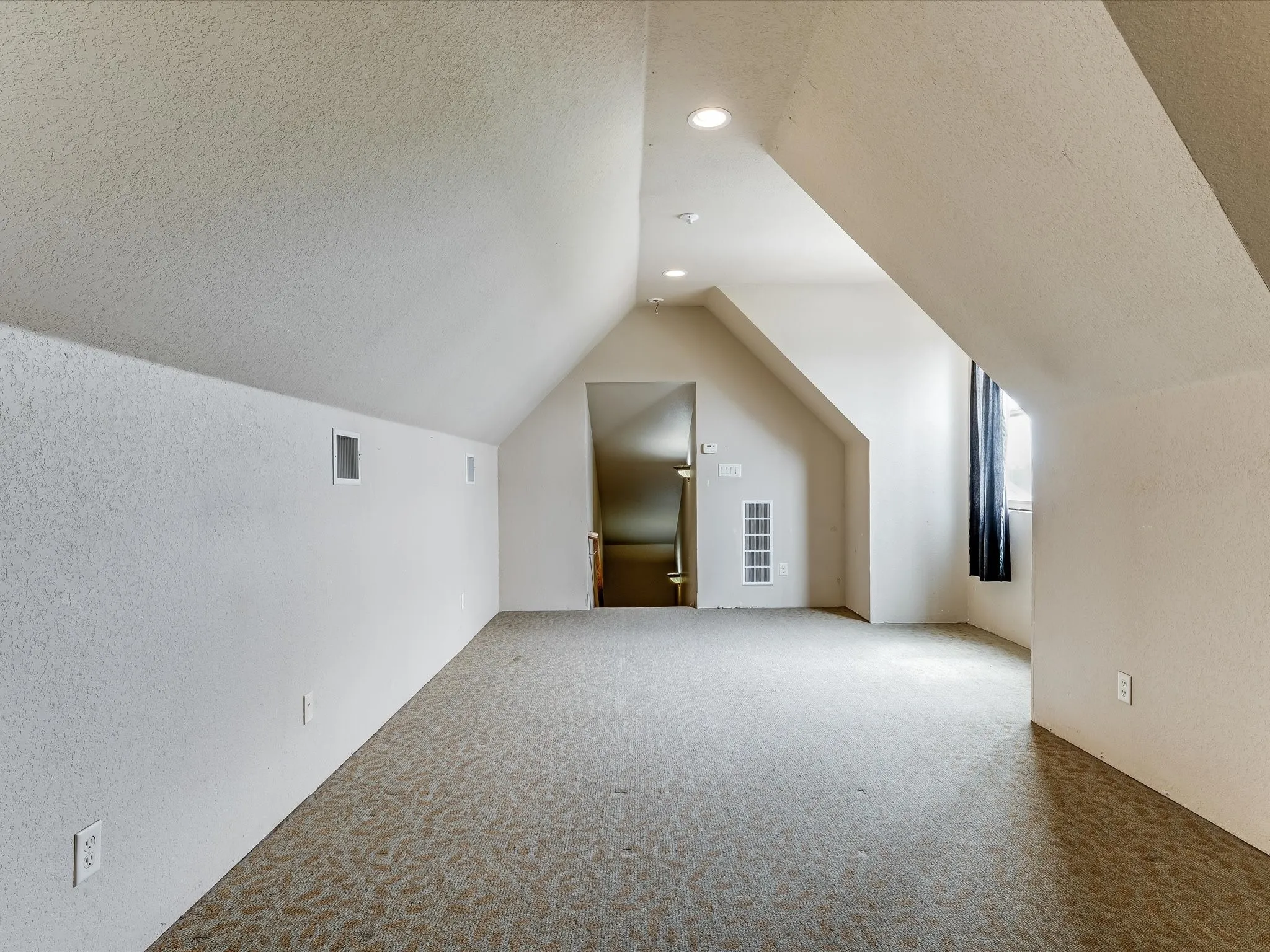 Spacious bonus room featuring sloped ceilings, recessed lighting, patterned carpeting, and a visible window