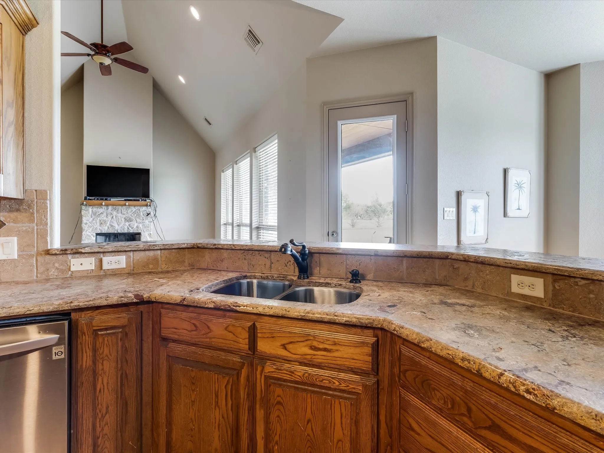 Kitchen featuring a double-basin stainless steel sink, wood-finish cabinetry, and stone countertops