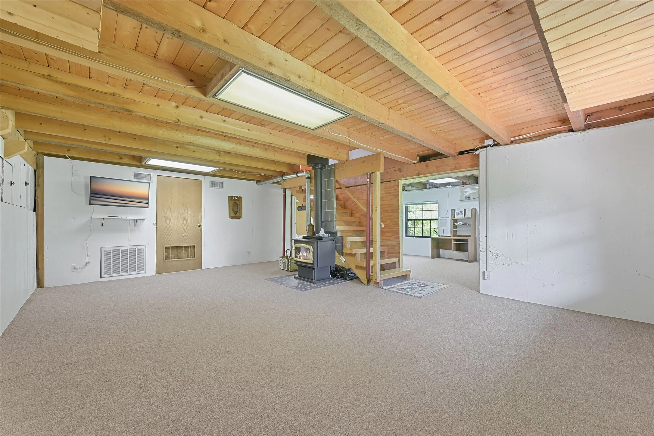 Lower Floor Living/Recreation Room. View of Small head Hi doors for storage to the left, Mechanical Room in the middle that is plumbed for a bath, Free Standing Wood Burning Stove, and Office Space, with walkout to Photographers back.