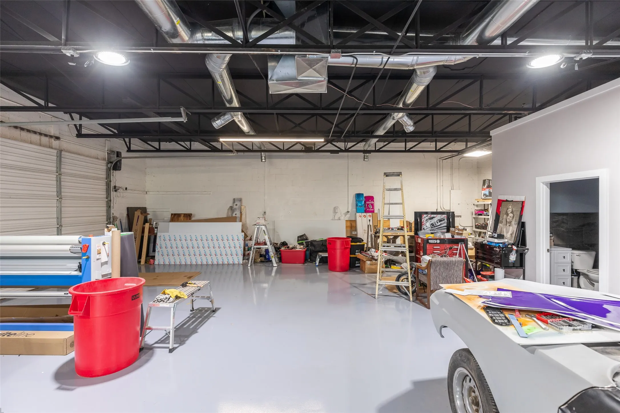 Spacious industrial interior featuring a high exposed ceiling with ductwork, multiple overhead lighting fixtures, and a light gray epoxy floor finish