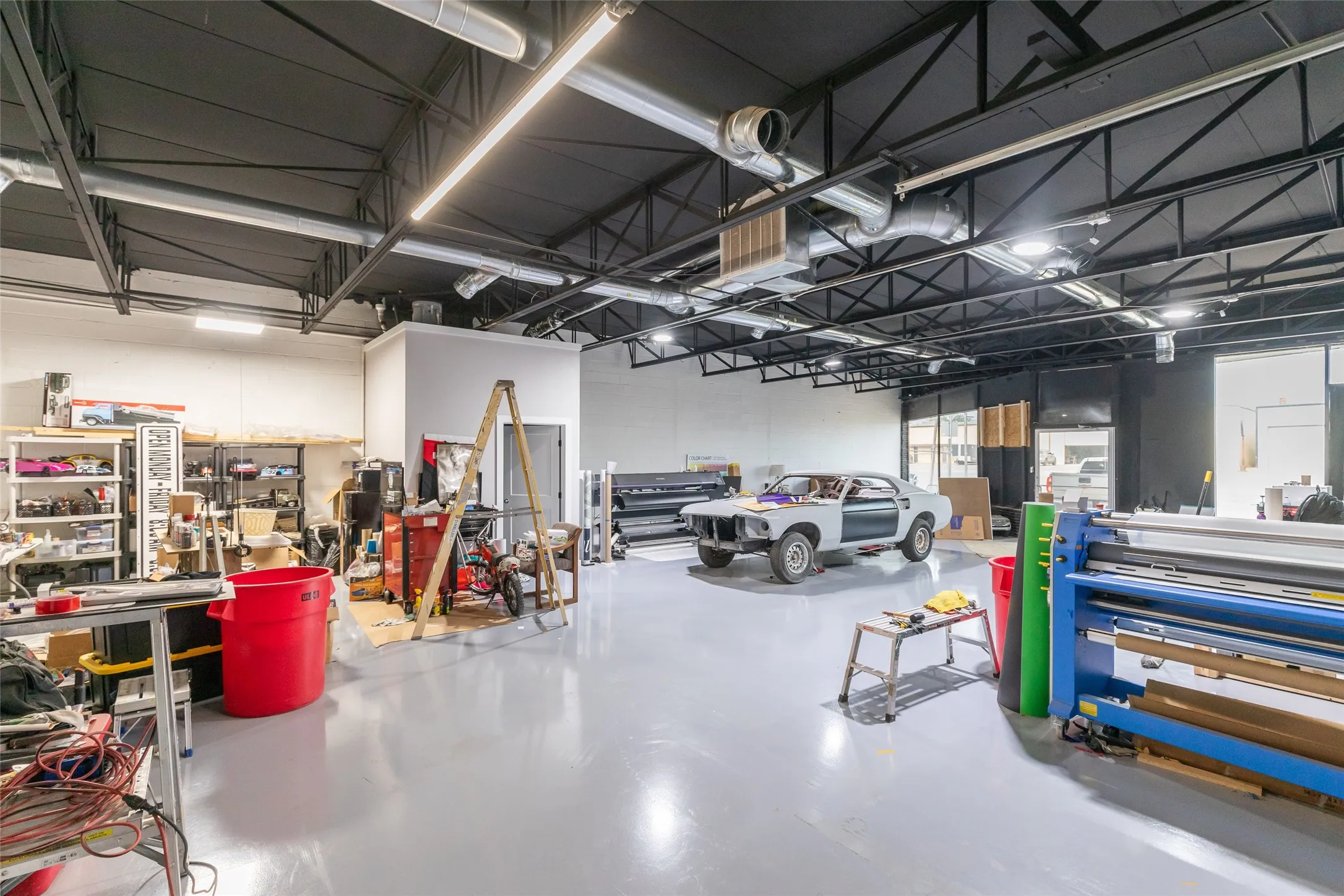 Spacious open-concept interior featuring a high exposed ceiling with black steel trusses, overhead fluorescent lighting, and visible ductwork