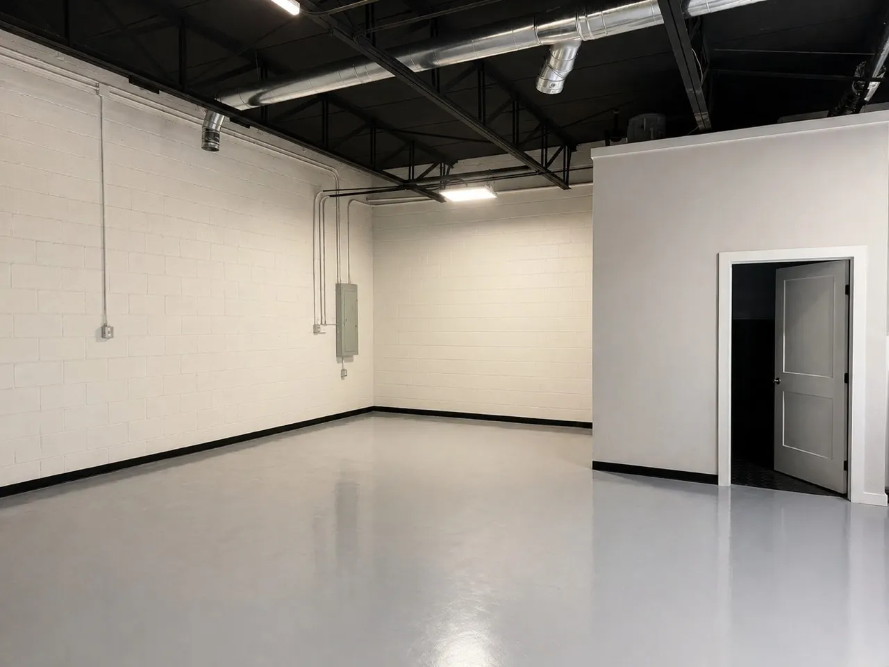Spacious interior featuring a light gray finished floor, exposed ceiling with black beams, white block walls, and modern overhead lighting