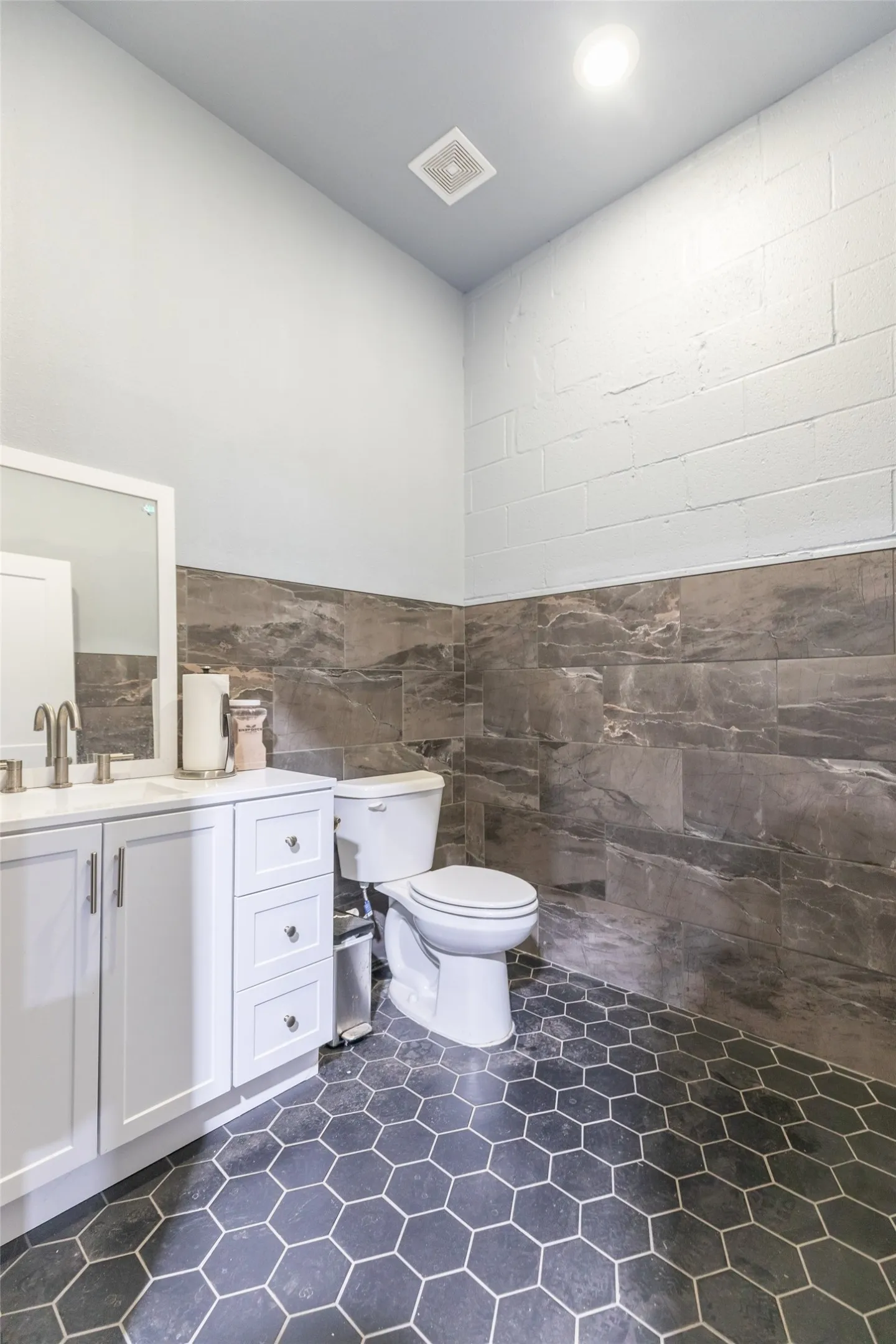 Powder room featuring hexagon tile flooring, white vanity with brushed nickel hardware, wall-mounted mirror, and dark gray stone-finish wall tile