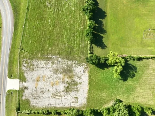 Expansive agricultural land featuring a paved road frontage, established tree lines, and a distinct cleared area