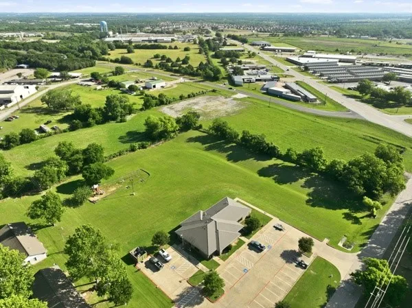 Single-story commercial building with a grey shingle roof and a spacious asphalt parking lot featuring multiple marked spaces