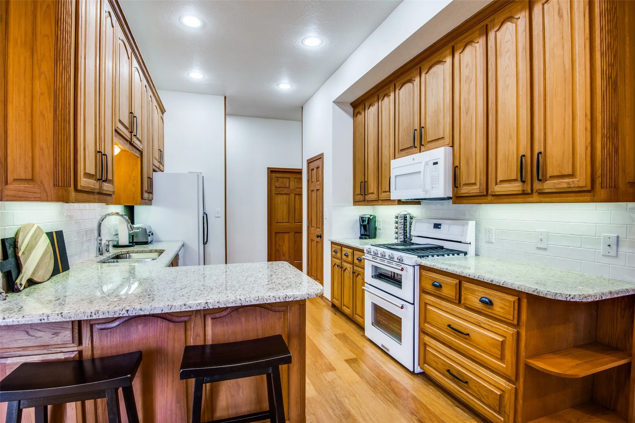 Kitchen featuring wood cabinetry, light-toned countertops, a white subway tile backsplash, stainless steel sink, and recessed lighting