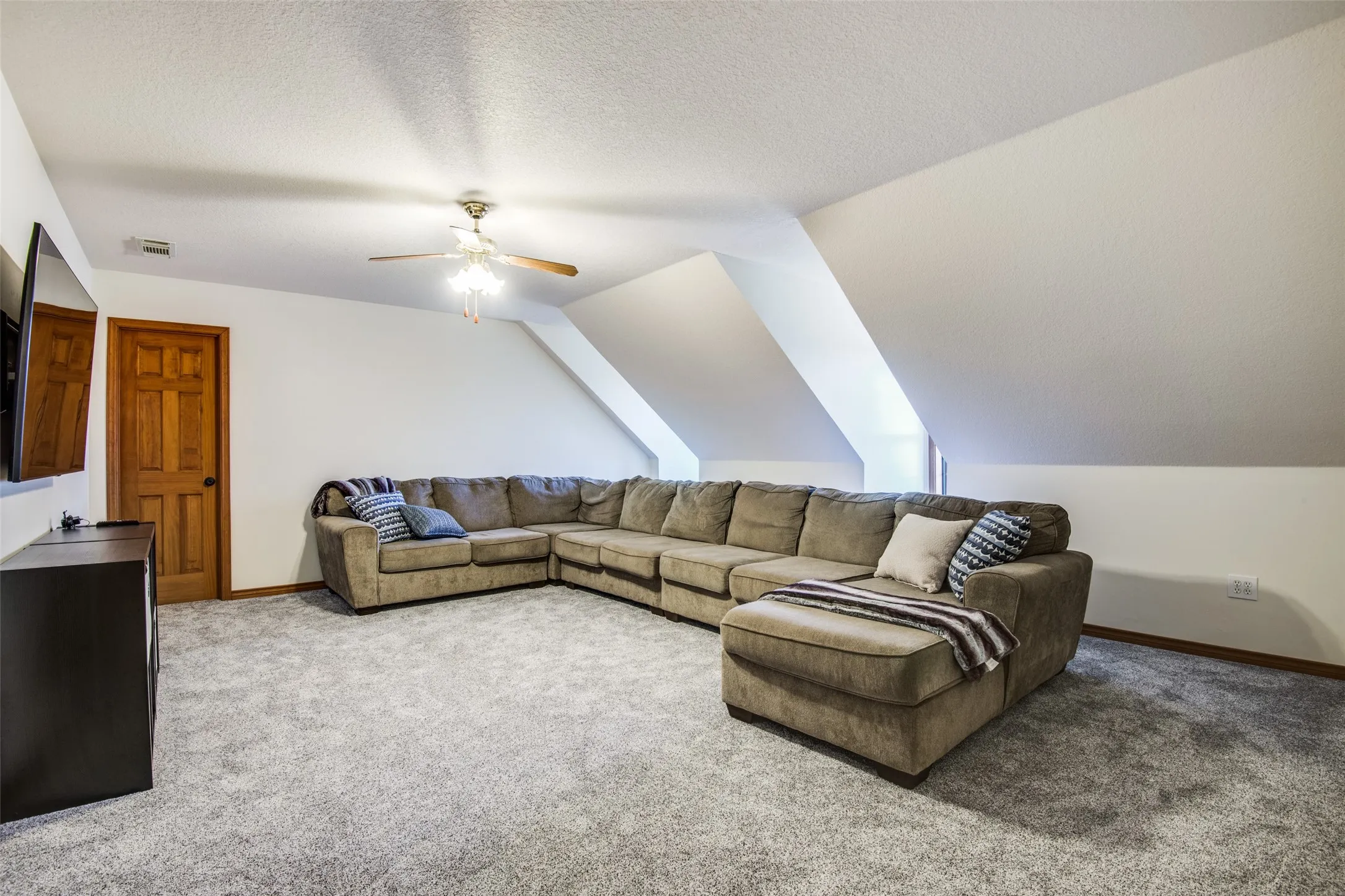 Spacious room featuring sloped ceilings, light gray carpet, a ceiling fan, and a wood-finish door