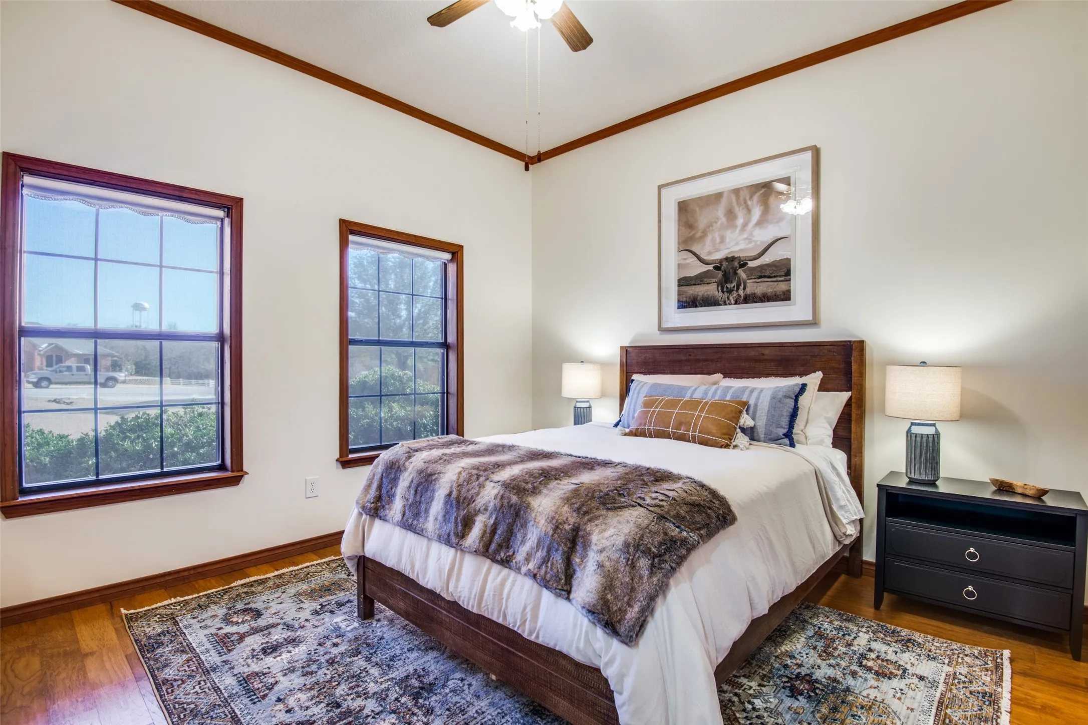 Bright room featuring wood-finish flooring, two window units with wood trim, and a ceiling fan with integrated lighting