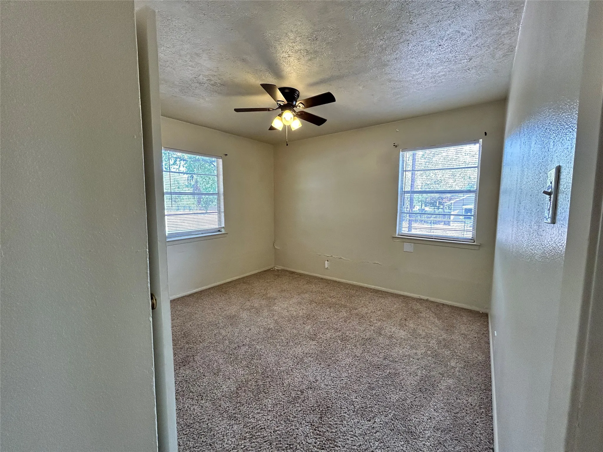 Carpeted room featuring two windows and a ceiling fan with integrated lighting