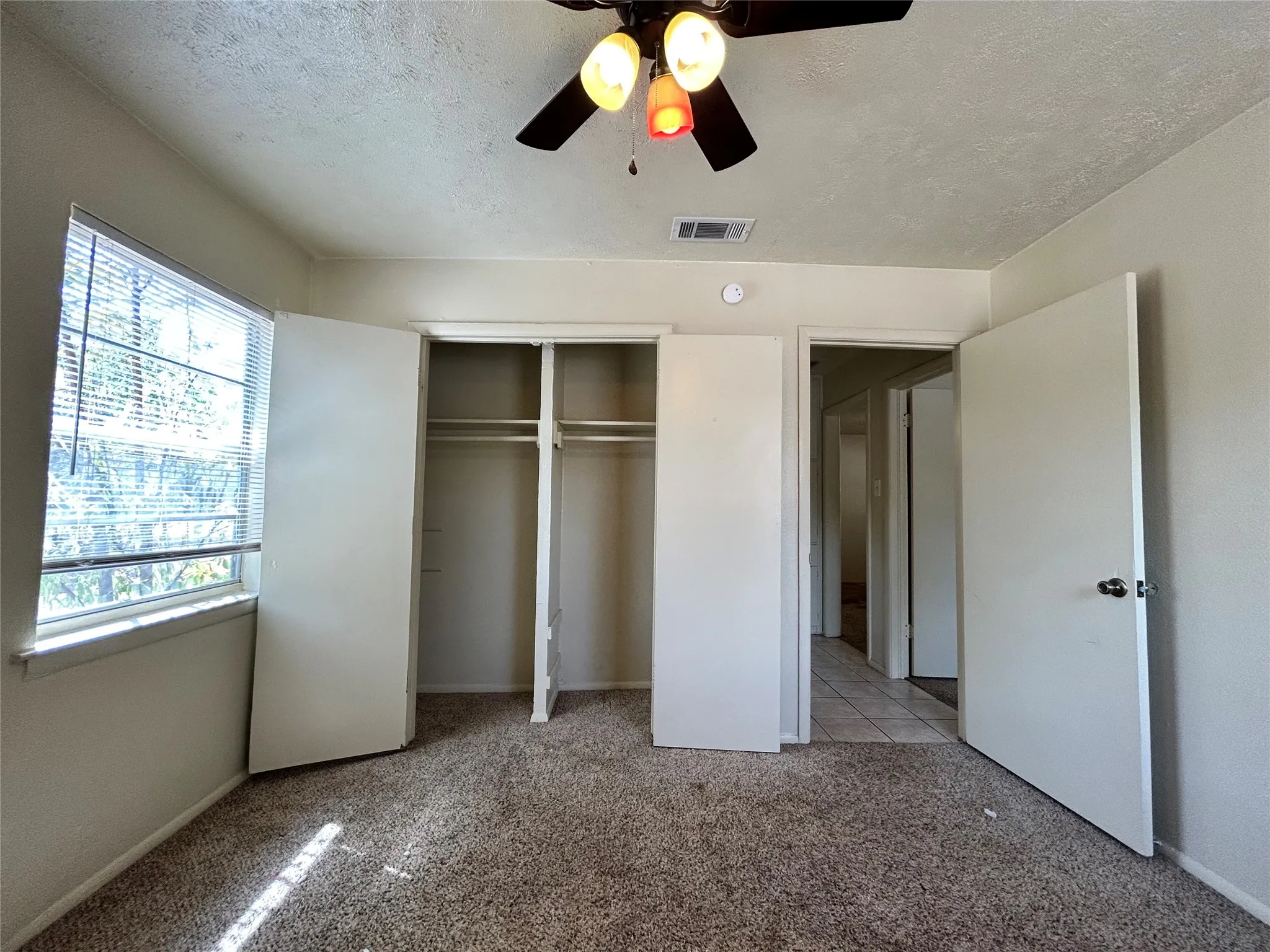 Carpeted room with a ceiling fan, window with blinds, and built-in closet with bi-fold doors