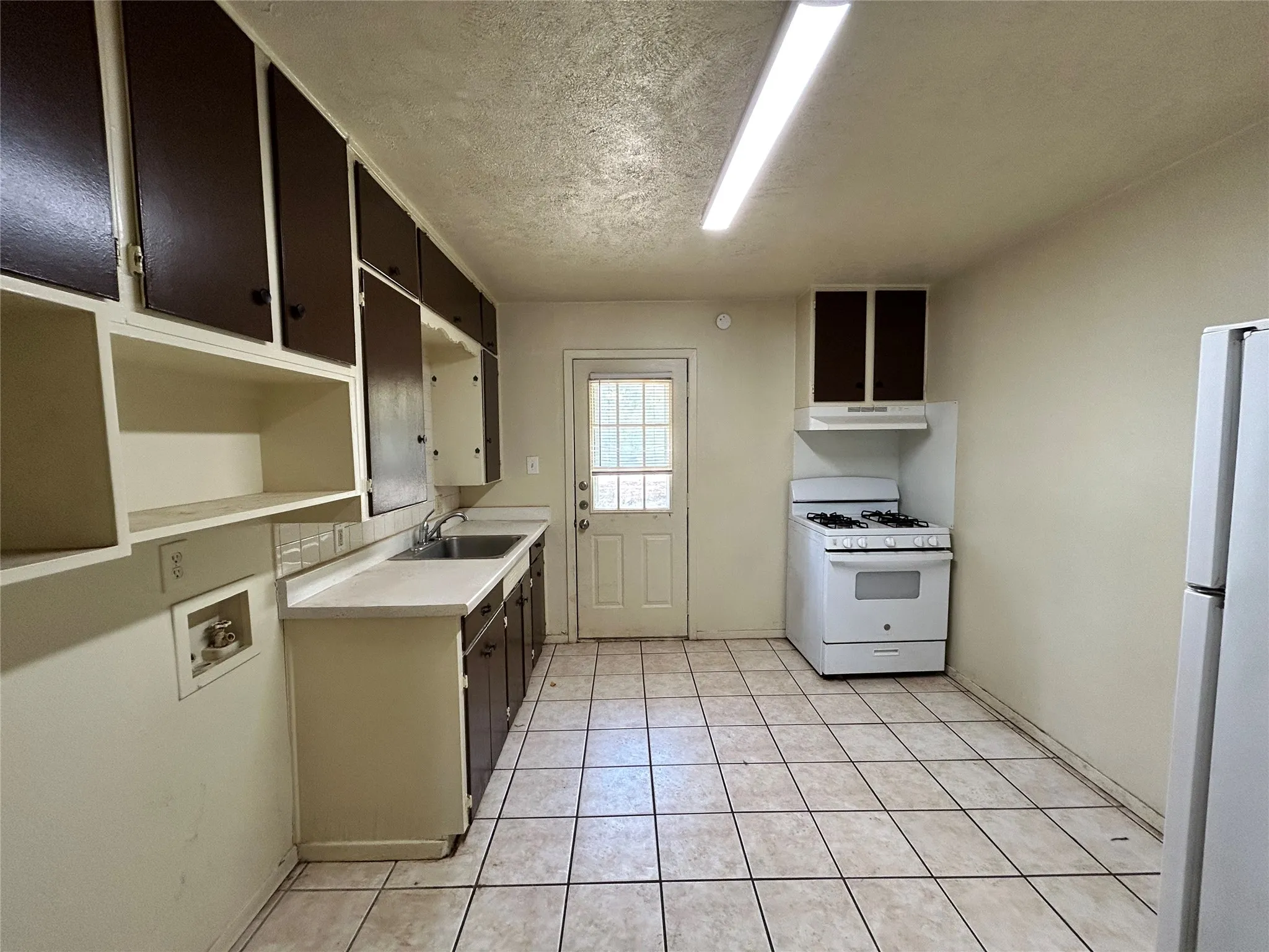 Kitchen featuring tiled flooring, a gas range, a single basin sink, and ample cabinetry