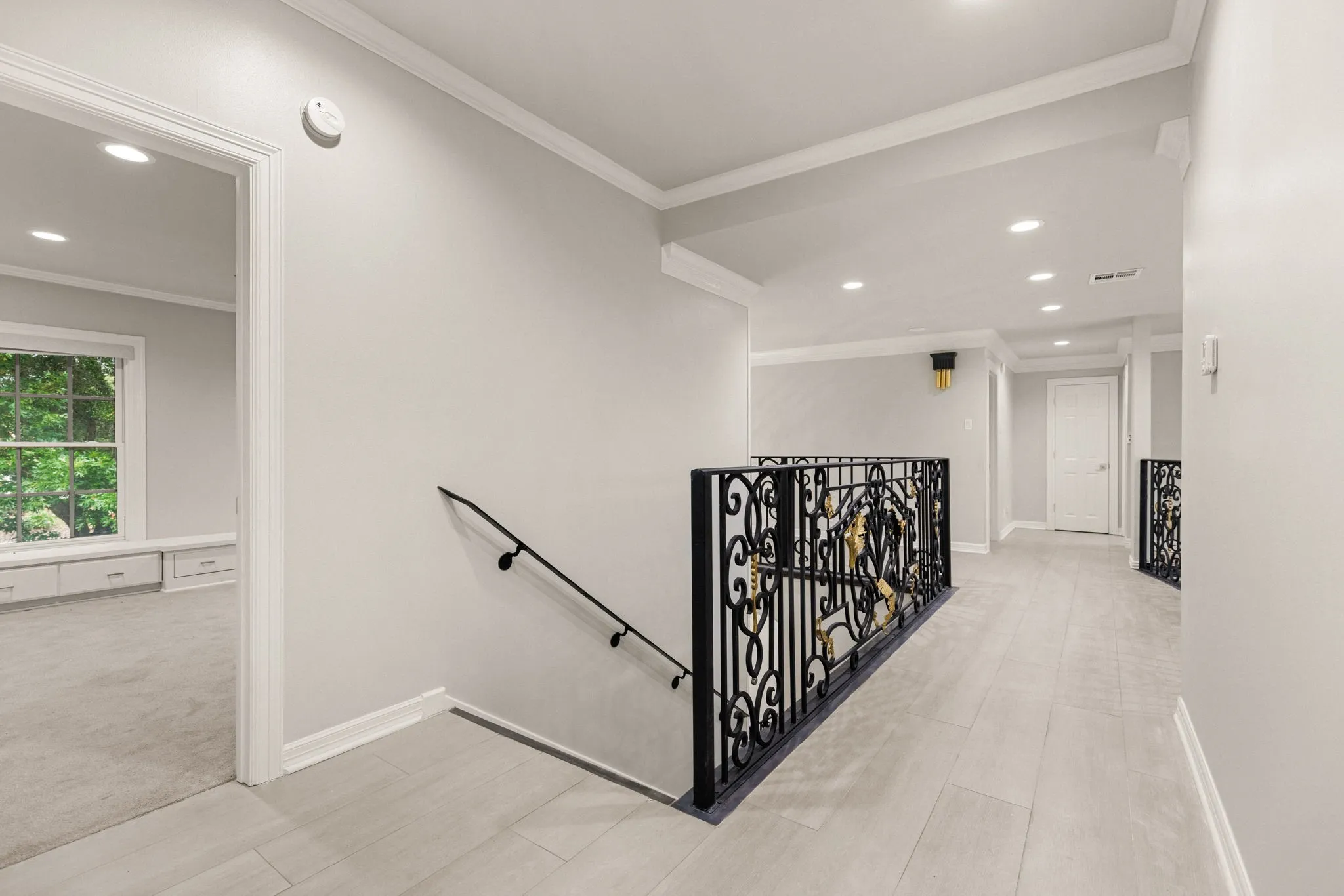 Upper-level hallway featuring light wood-finish flooring, recessed lighting, crown molding, and decorative wrought iron railings