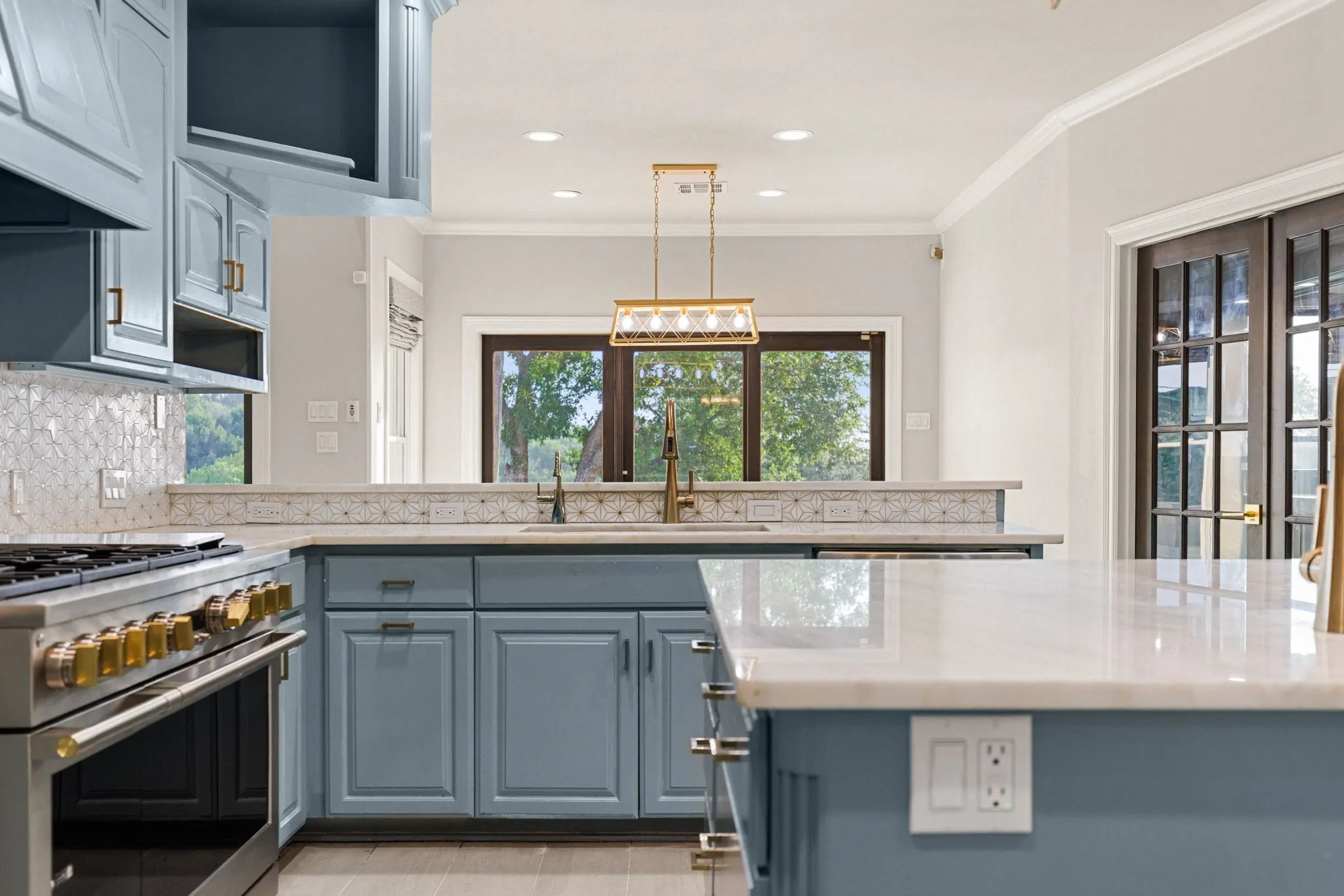 Kitchen featuring light blue cabinetry, white countertops, a mosaic tile backsplash, and stainless steel appliances with gold-tone hardware
