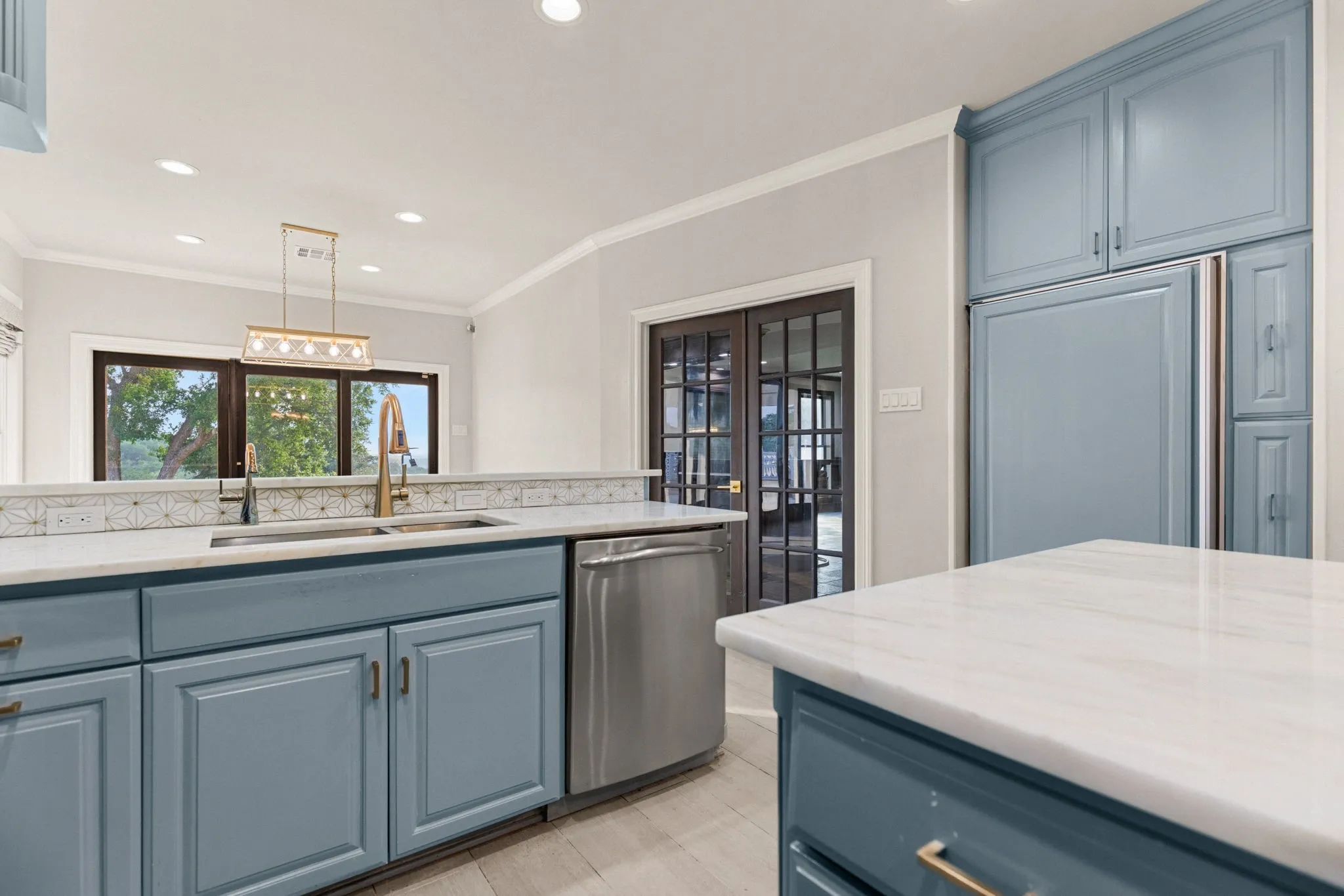 Kitchen featuring light blue cabinetry, integrated refrigerator, stainless steel dishwasher, and light-toned countertops