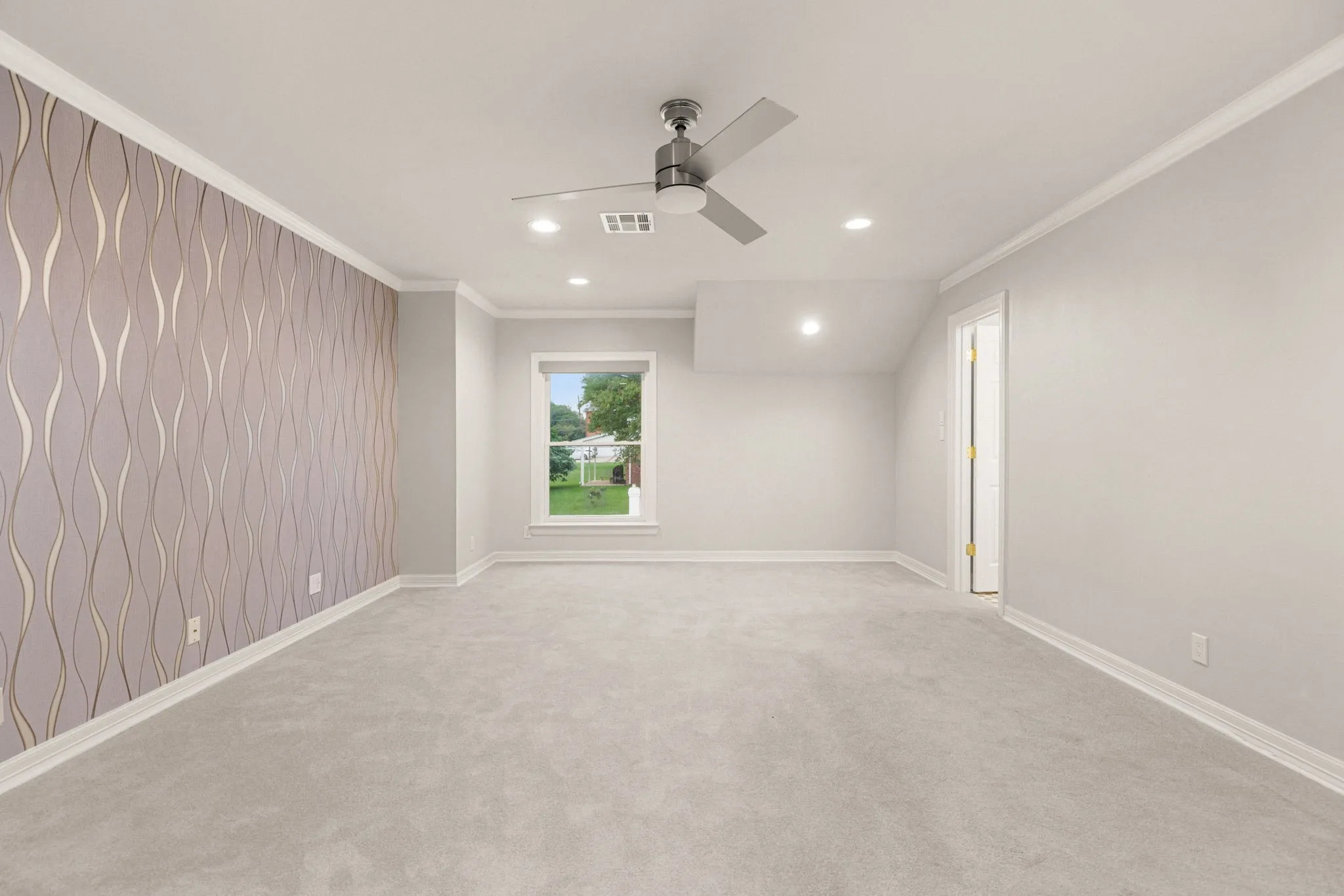 Spacious room featuring a decorative accent wall, light grey carpeting, recessed lighting, a ceiling fan, and white trim