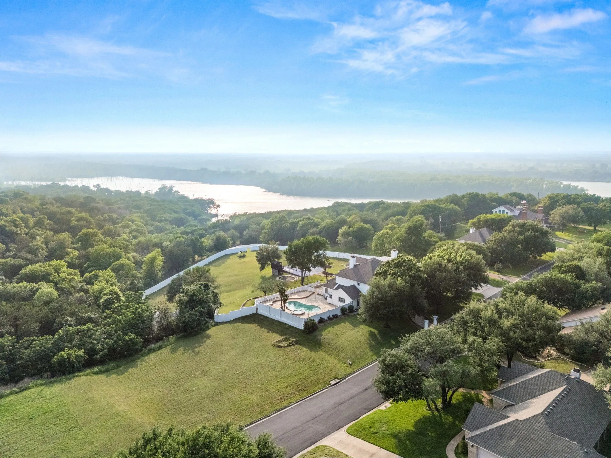 Expansive property featuring a white residence with a private swimming pool, surrounded by mature trees and a manicured lawn