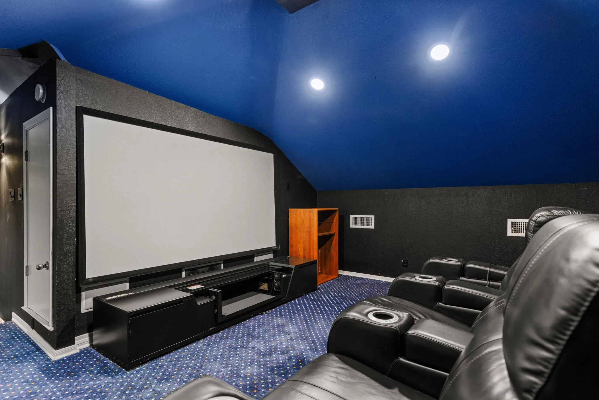 Dedicated media room featuring a large projection screen, dark textured walls, and a blue acoustic ceiling