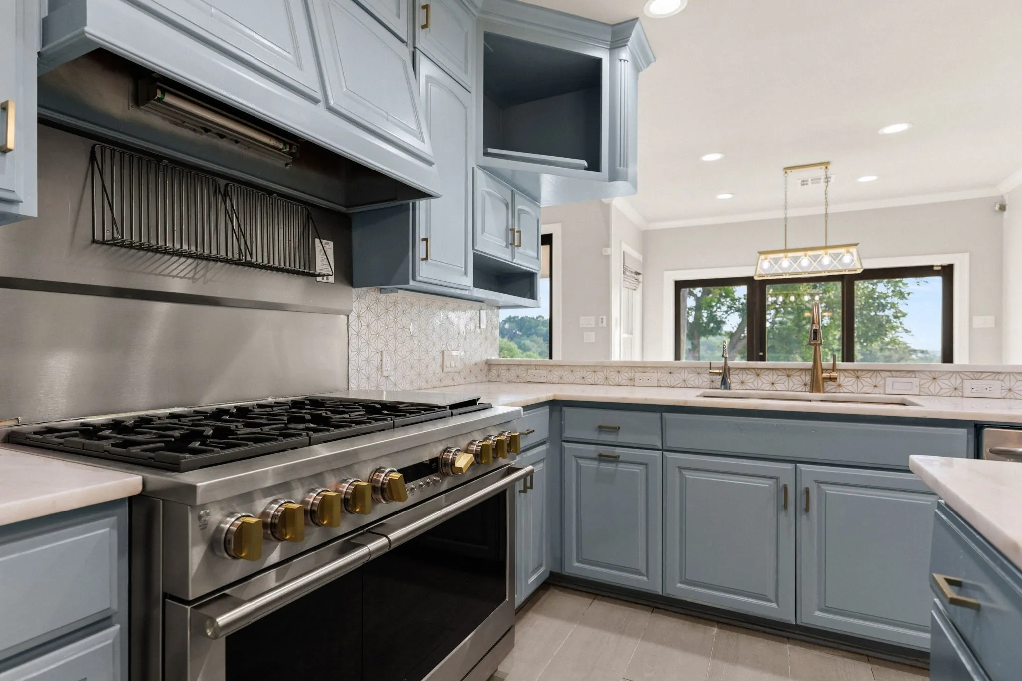 Gourmet kitchen featuring a professional-grade range with stainless steel backsplash, custom blue cabinetry, light-toned countertops, and decorative tile accents