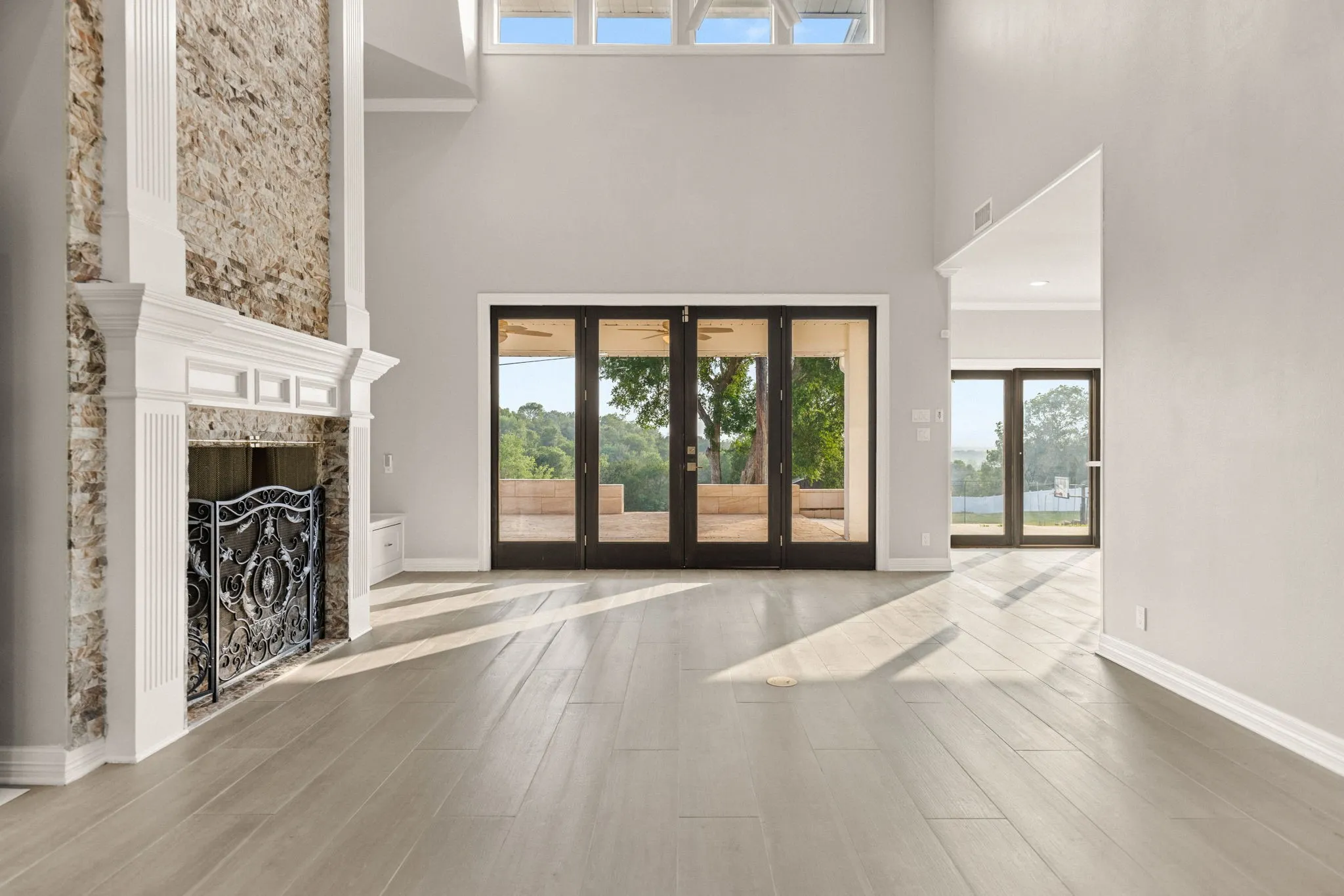 Spacious living area featuring high ceilings, wood-finish flooring, a stone-clad fireplace with a white mantel, and multiple sets of glass-paneled double doors