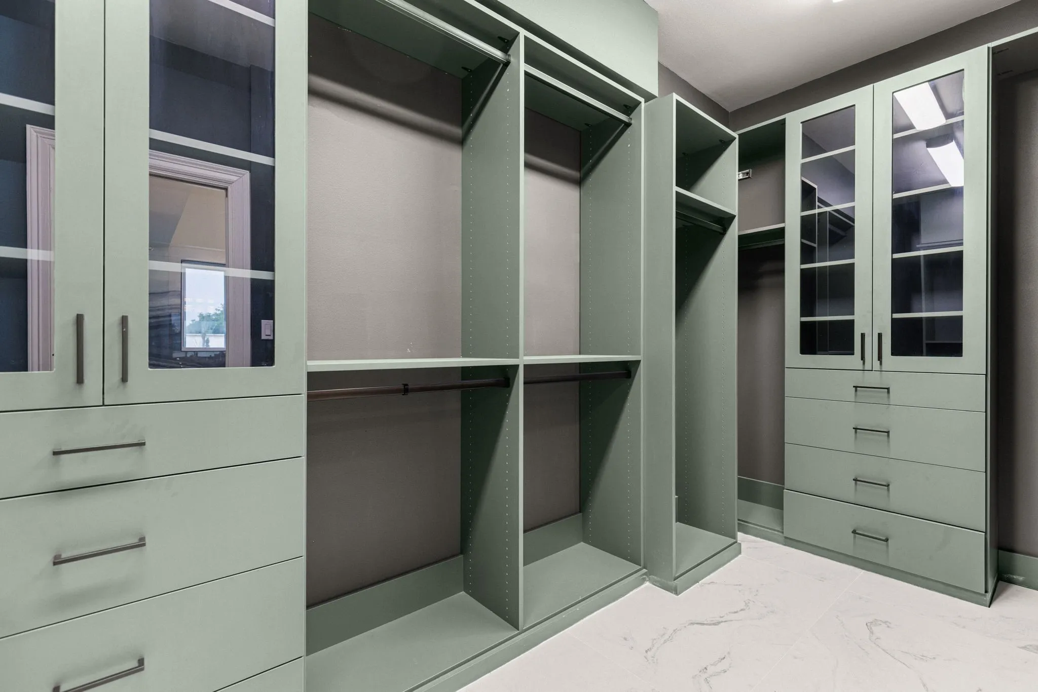 Custom closet system featuring glass-front cabinetry, multiple hanging rods, built-in shelving, and integrated drawers