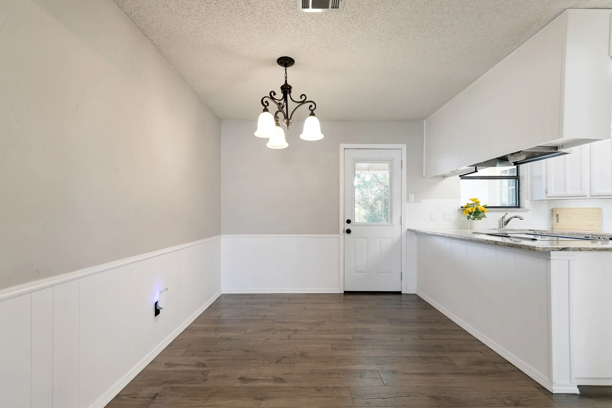 Dining area featuring wood-finish flooring, white wainscoting, and a multi-arm chandelier