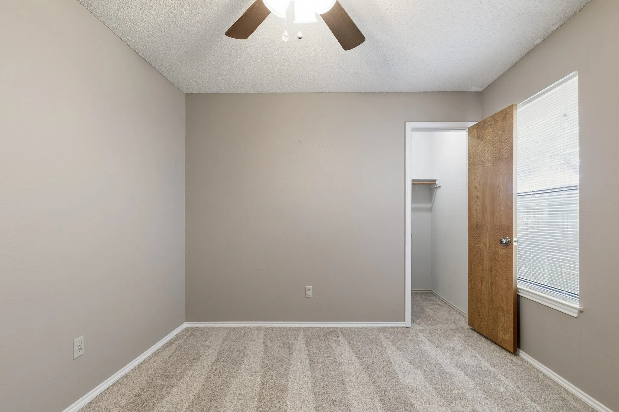 Bedroom featuring neutral-toned walls, patterned carpeting, a ceiling fan with integrated lighting, a window with blinds, and an open closet with shelving and wood-finish flooring