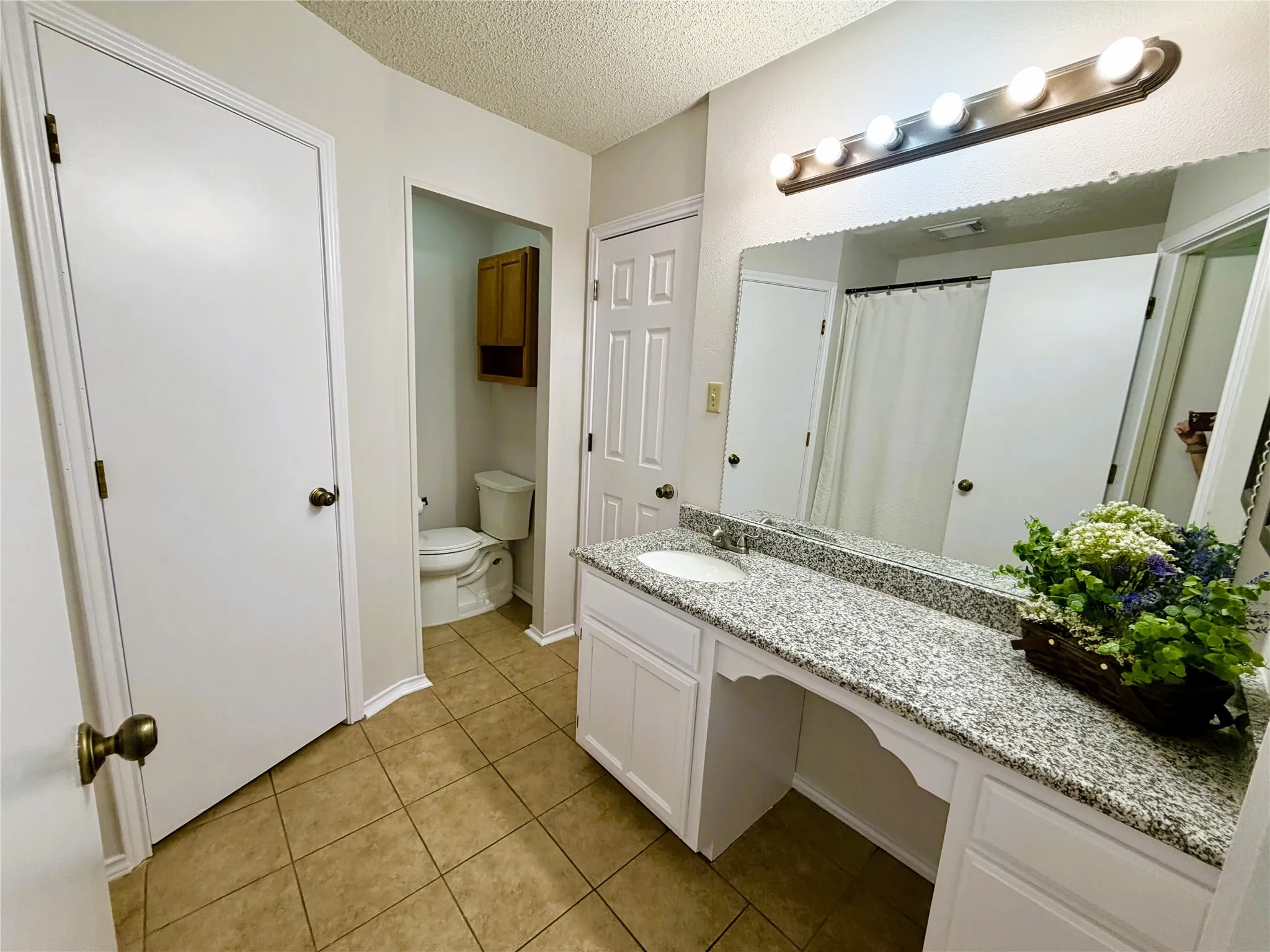 Bathroom vanity featuring a granite-style countertop with an integrated sink, white cabinetry, a large wall-mounted mirror, and tile flooring