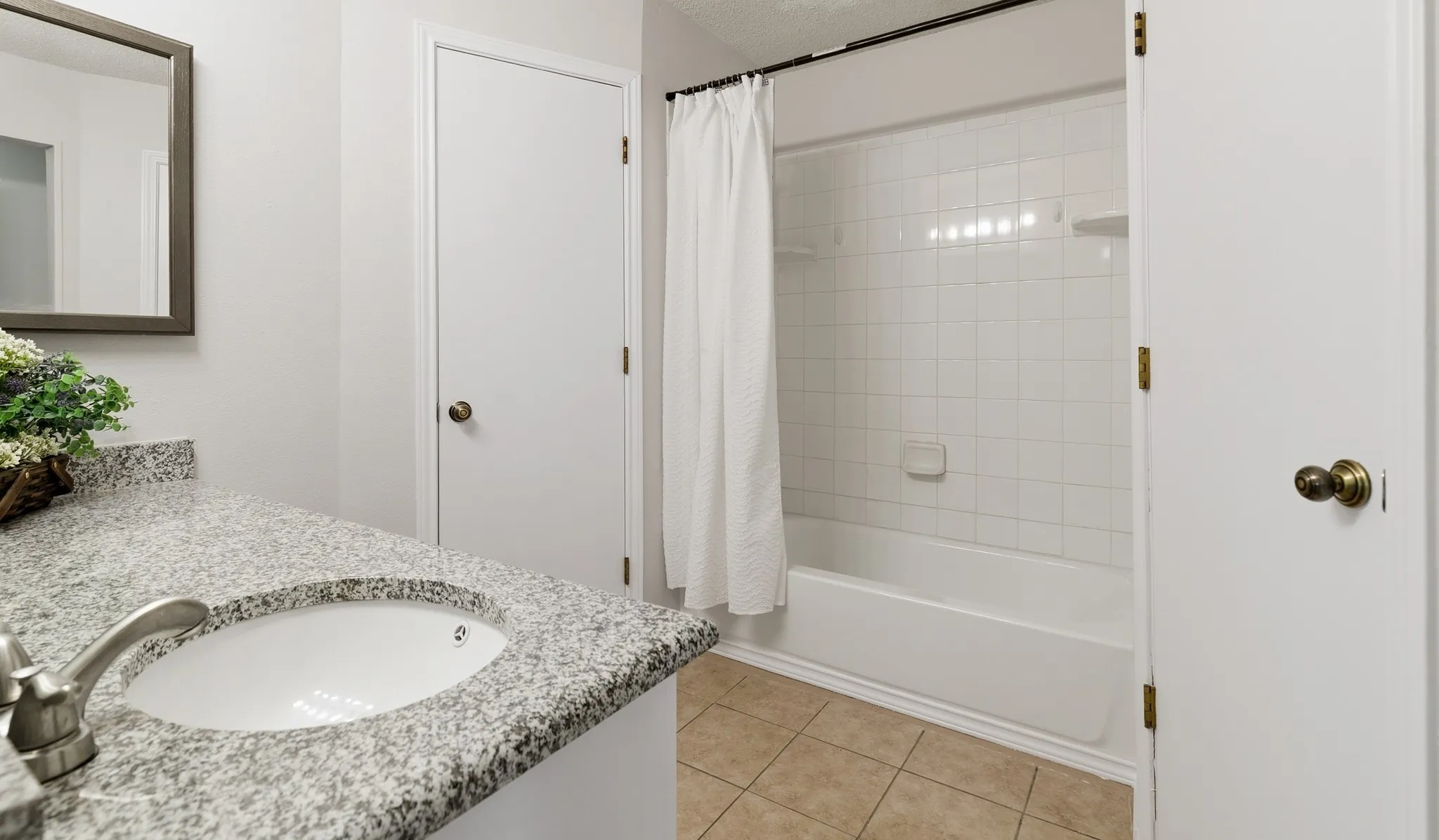 Bathroom featuring a white subway tile tub surround, an undermount sink, a granite-finish countertop, and tan tile flooring