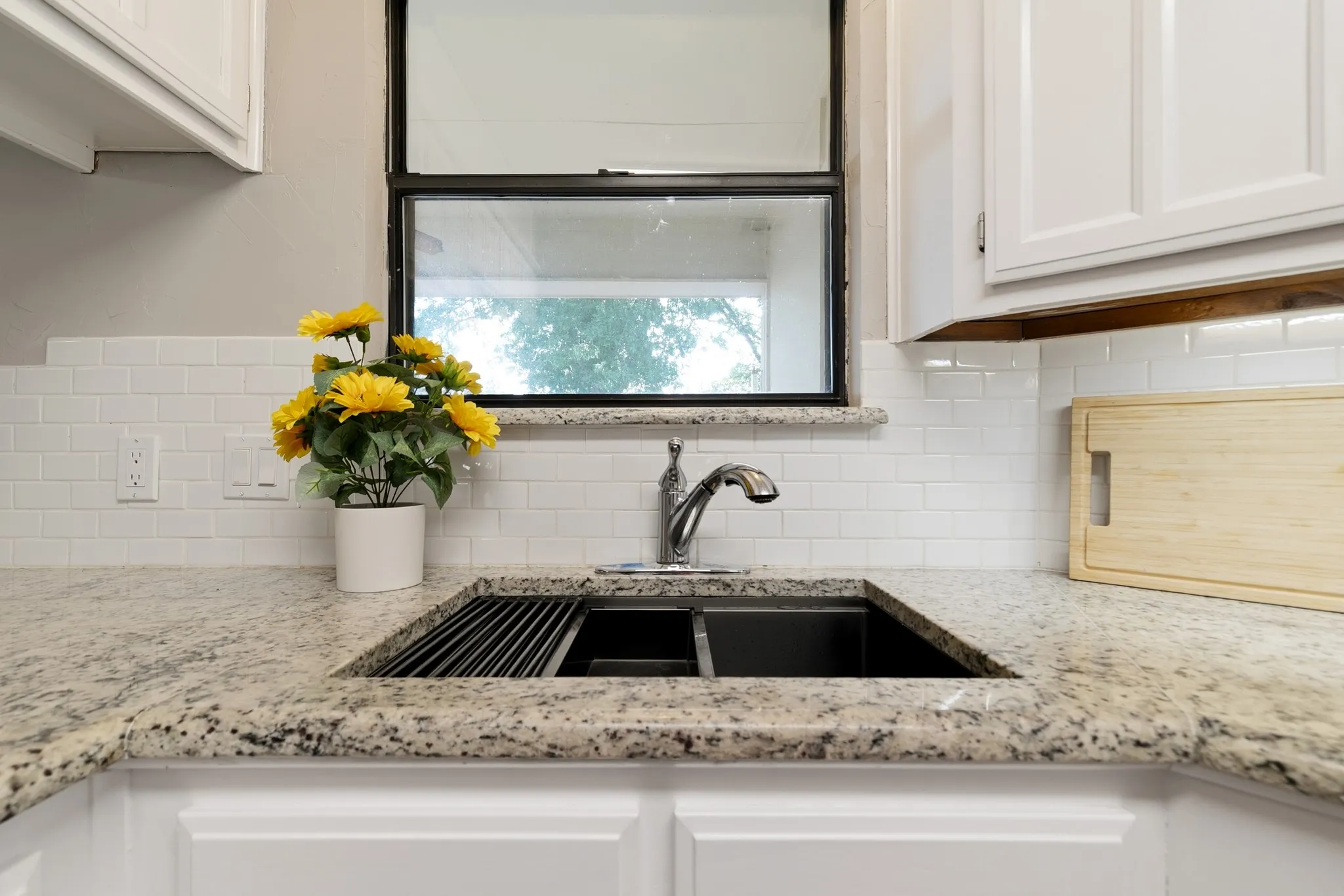 Kitchen sink featuring a dual-basin workstation sink with integrated drying rack, a gooseneck faucet, light-toned granite countertops, white subway tile backsplash, and white cabinetry