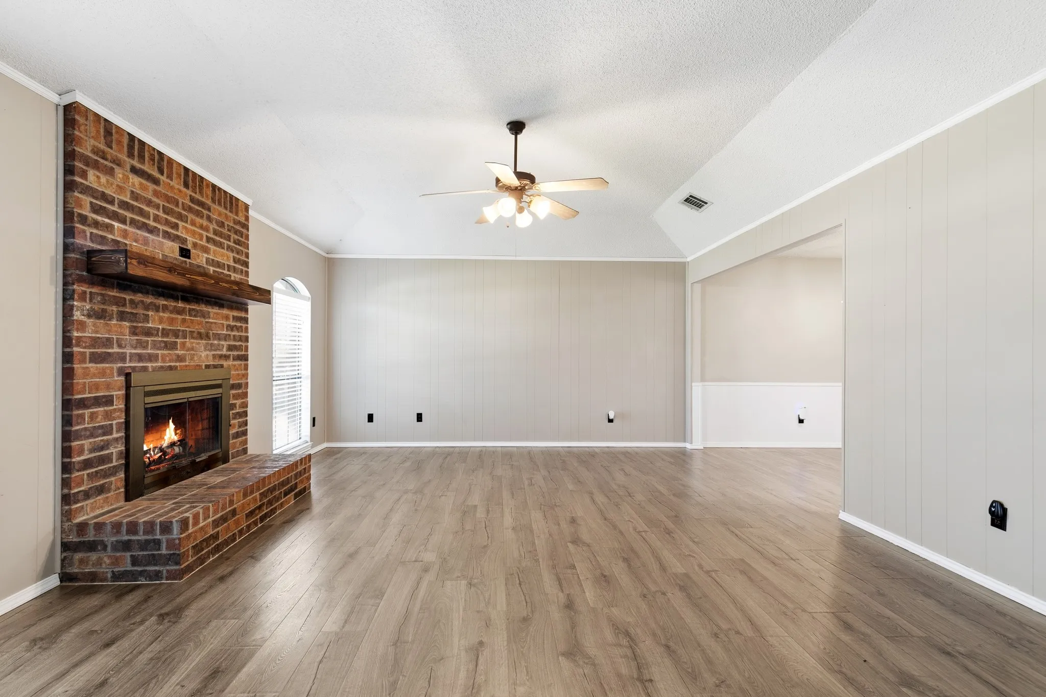 Spacious room featuring wood-finish flooring, a brick fireplace with a wood mantle, vaulted ceilings, and a ceiling fan