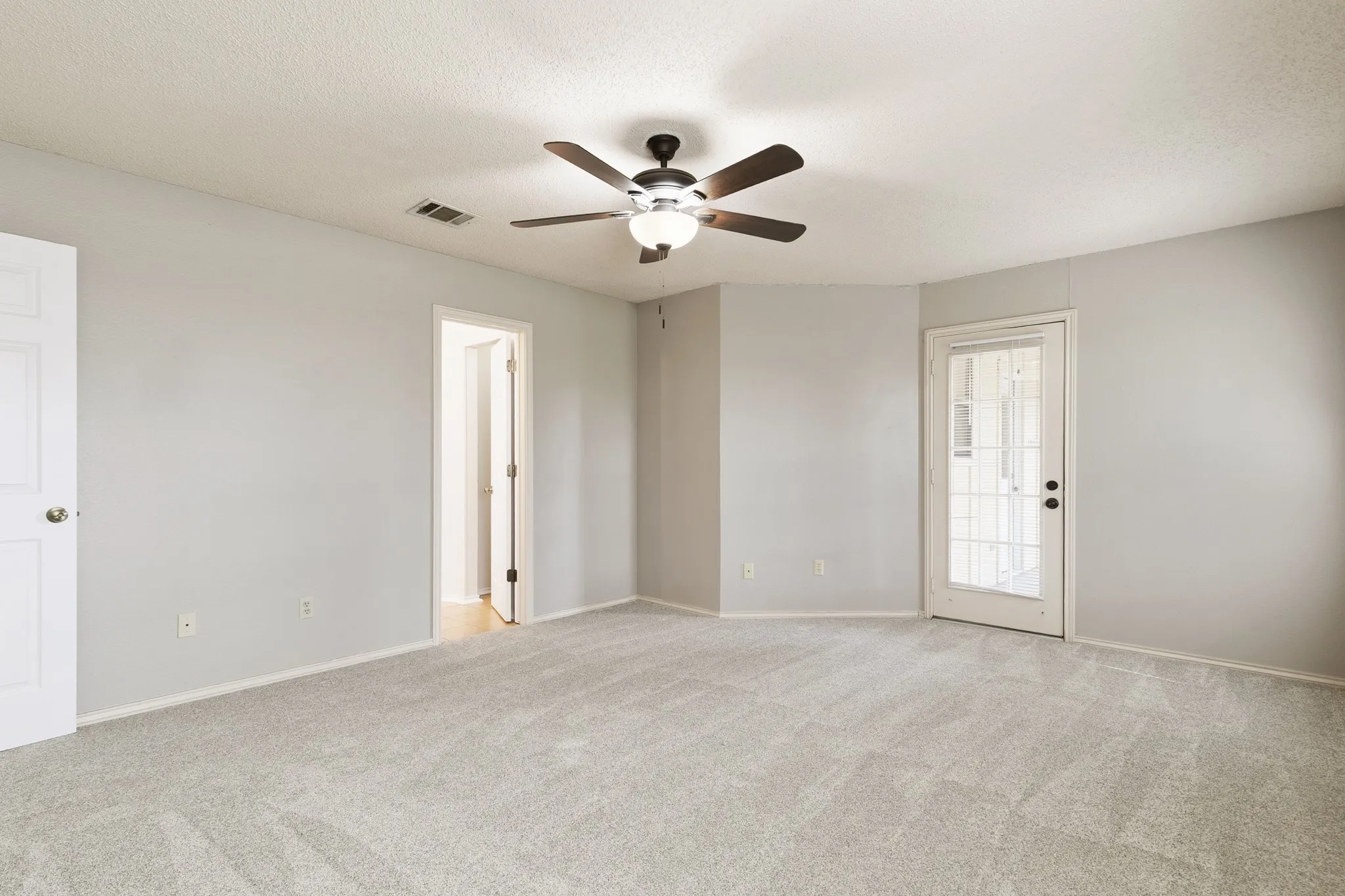 Spacious room featuring light gray carpeting, neutral wall paint, and a ceiling fan with integrated lighting