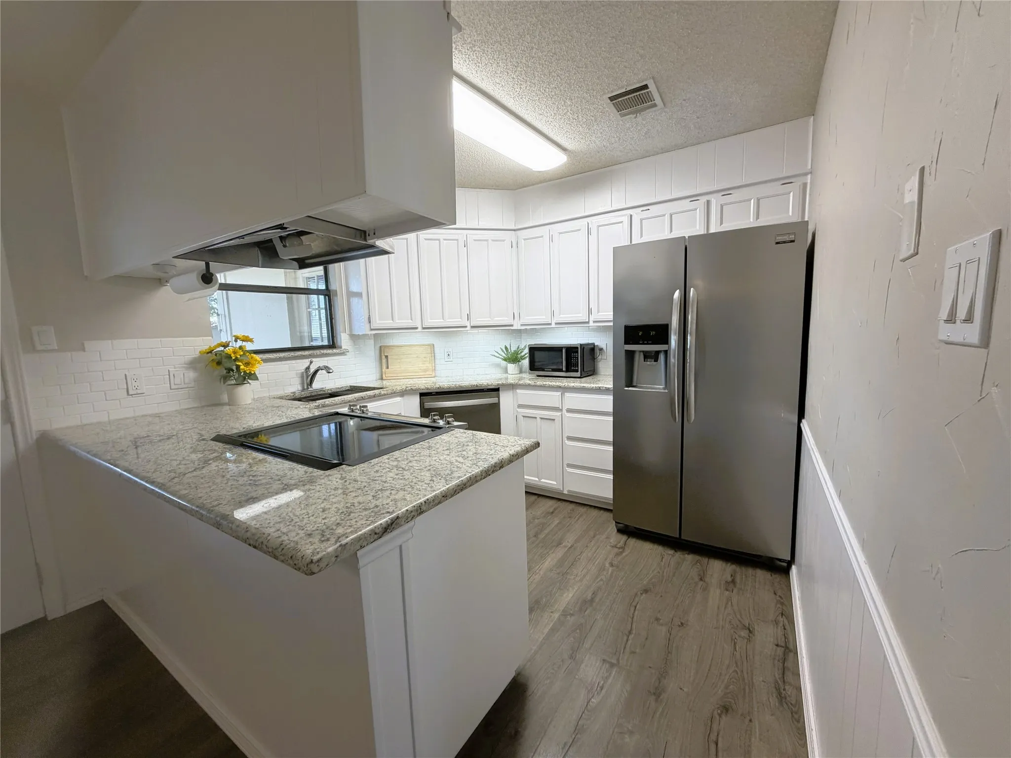 White cabinetry, granite countertops, tile backsplash, stainless steel appliances, and wood-finish flooring