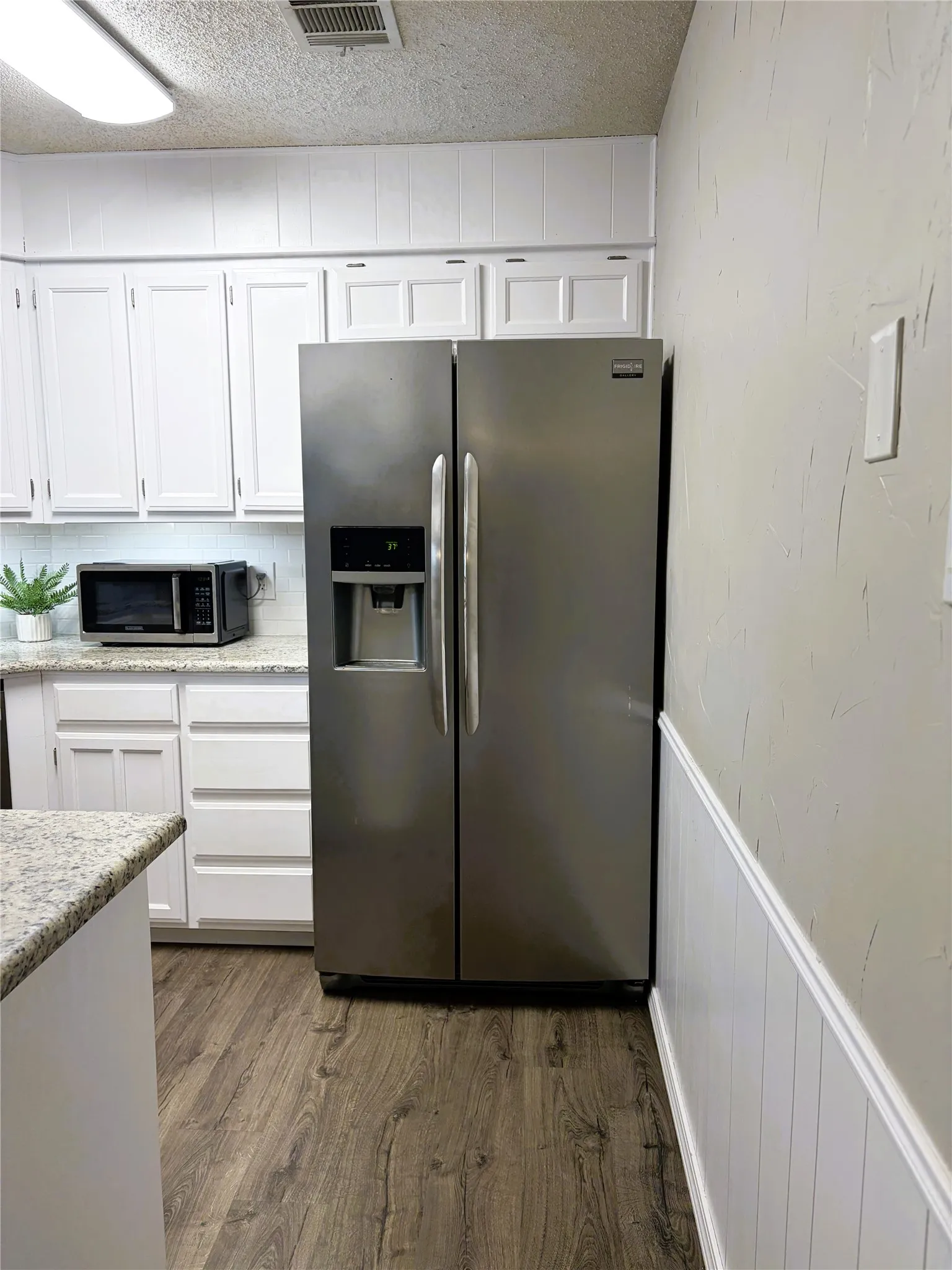 White cabinetry, wood-finish flooring, stainless steel refrigerator, light-colored countertops, and white paneling