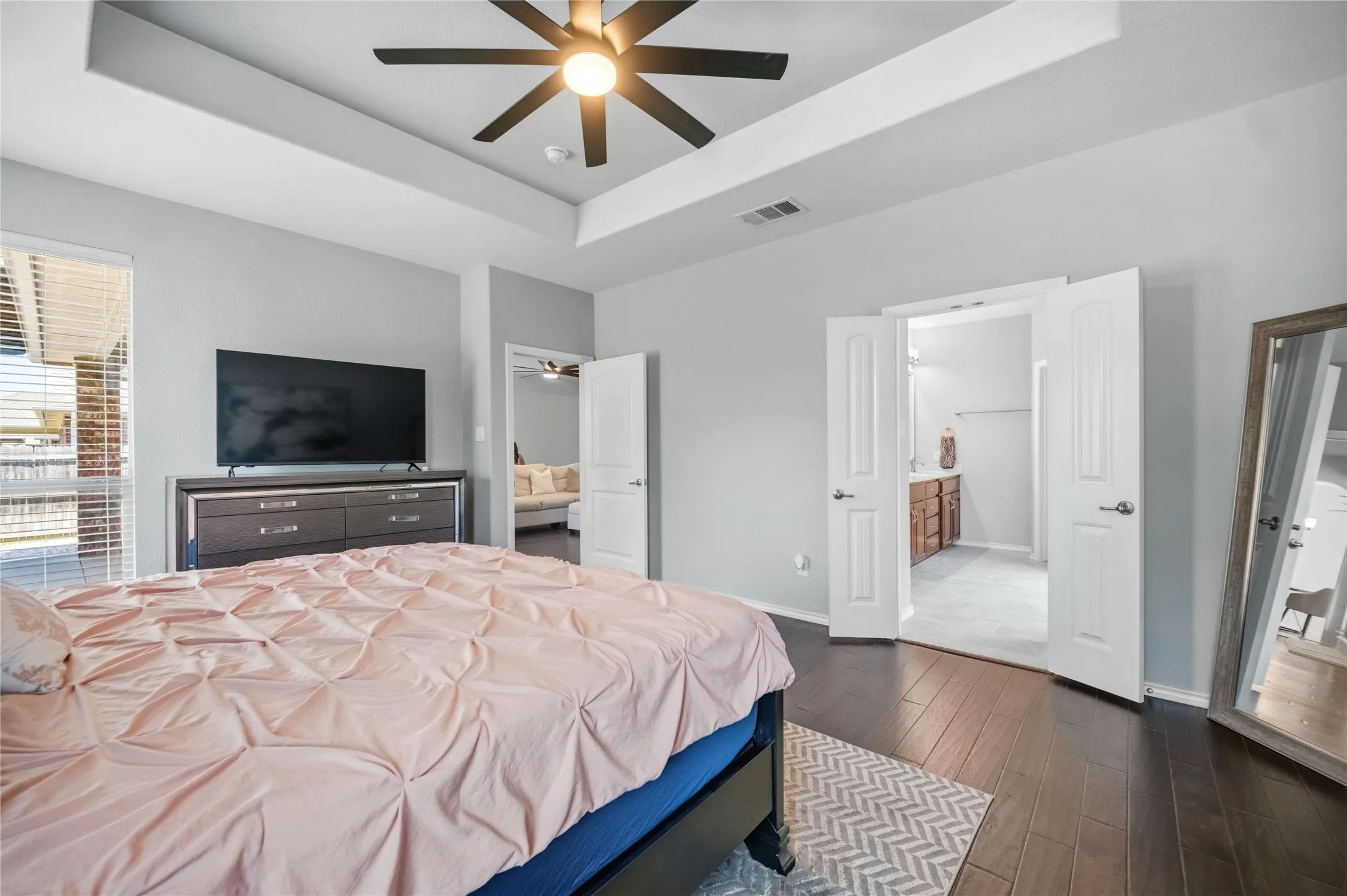 Tray ceiling with a ceiling fan light fixture, dark wood-finish flooring, and light gray wall paint