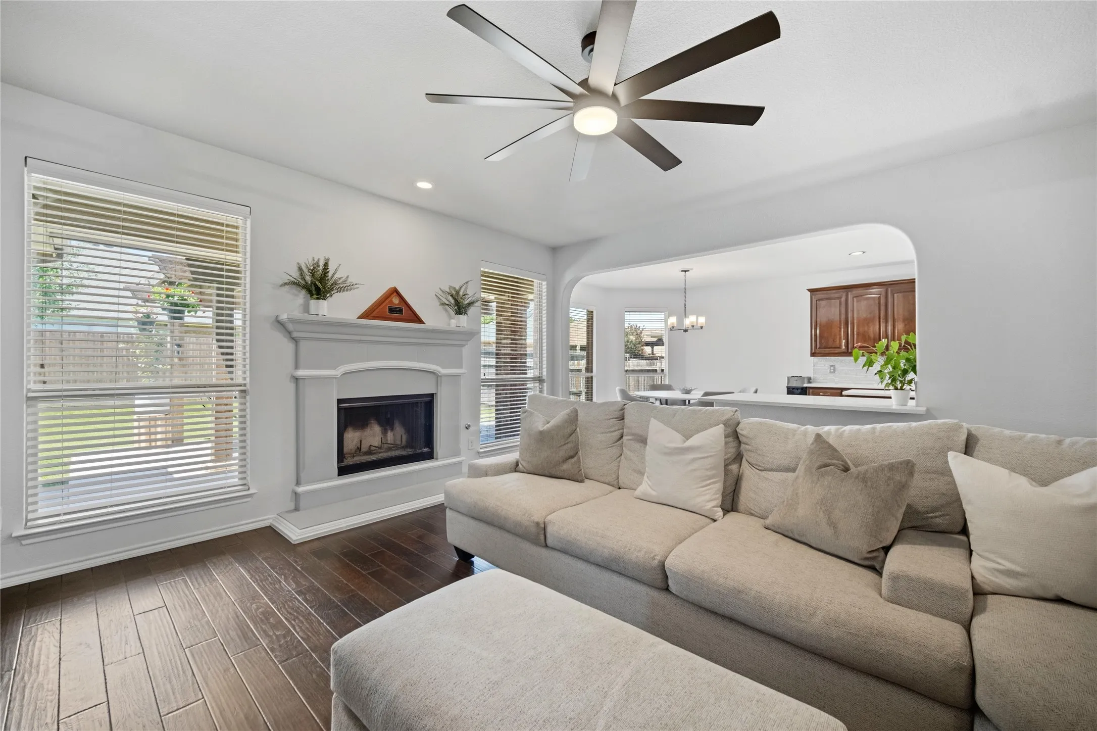 Living area featuring a white mantel fireplace, wood-finish flooring, and a modern ceiling fan