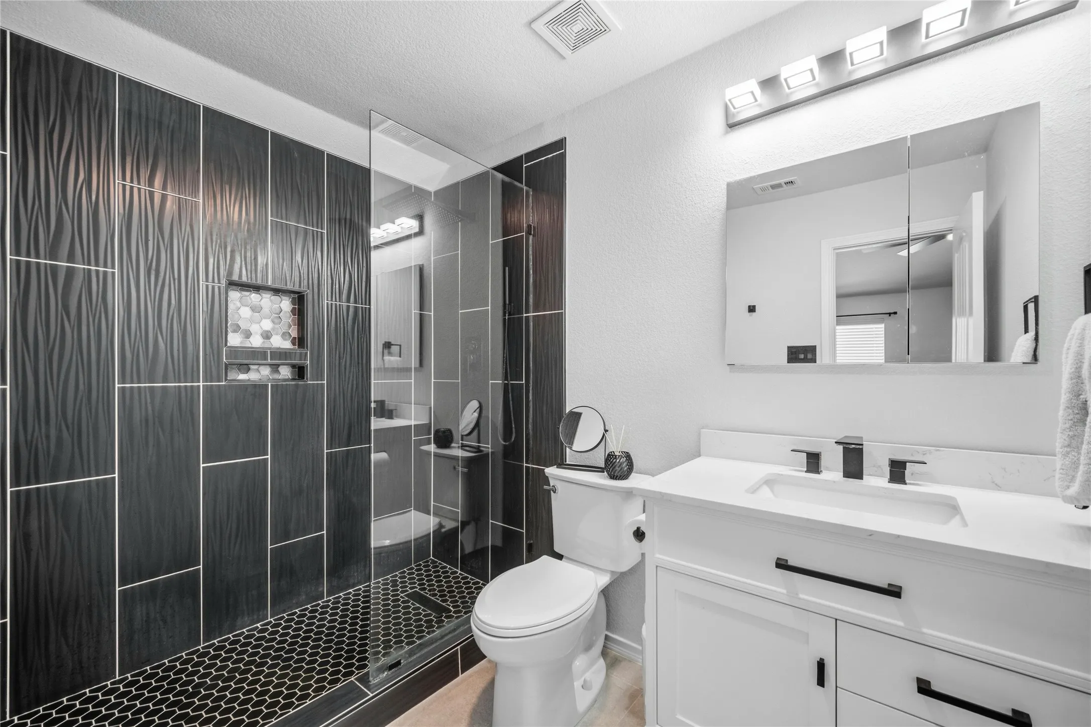 Modern bathroom featuring a walk-in shower with textured dark tile walls and hexagonal floor tiles