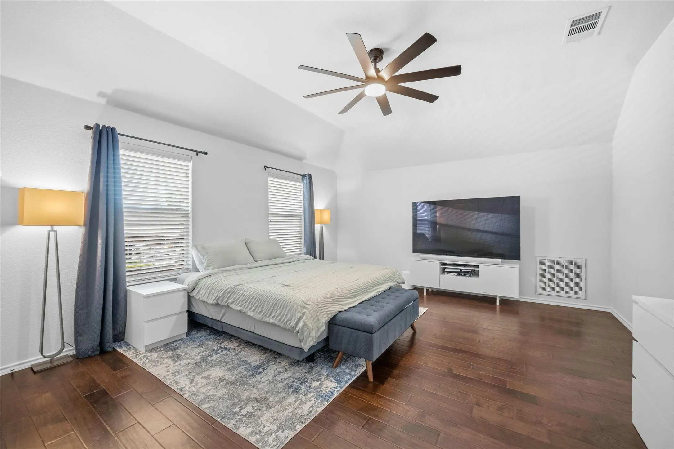 Spacious bedroom featuring wood-finish flooring, vaulted ceiling, and two windows with blinds