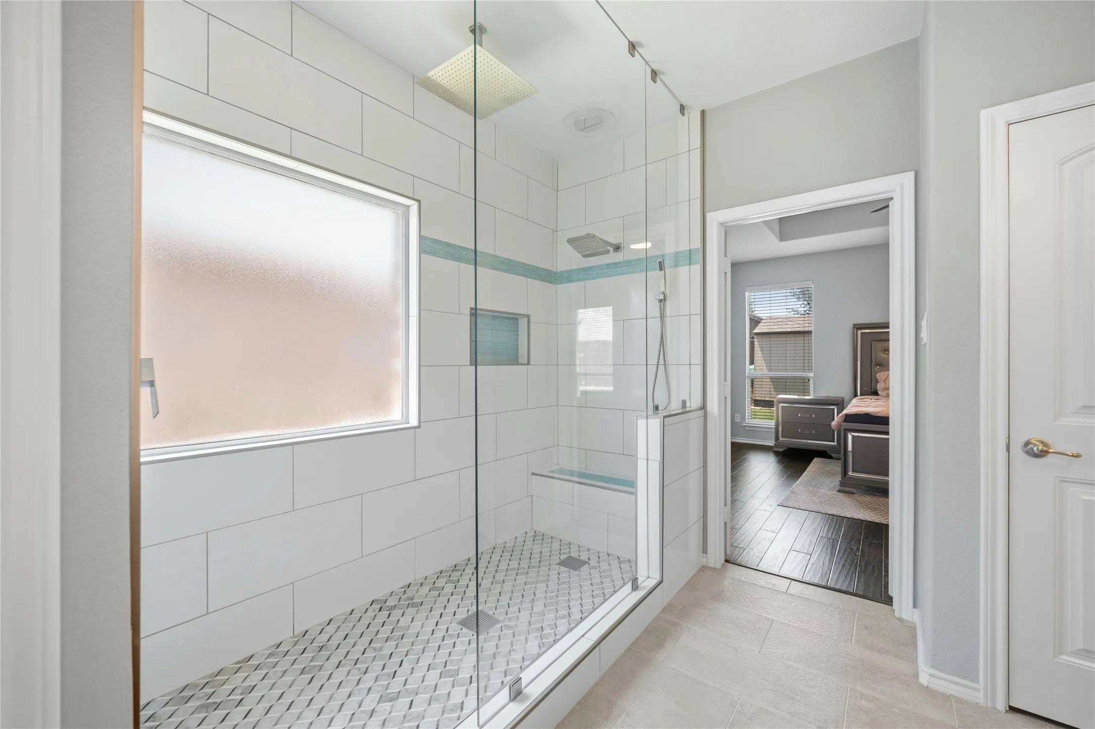 Spacious glass-enclosed shower with white subway tile, mosaic floor tile, built-in bench, and a rectangular frosted window